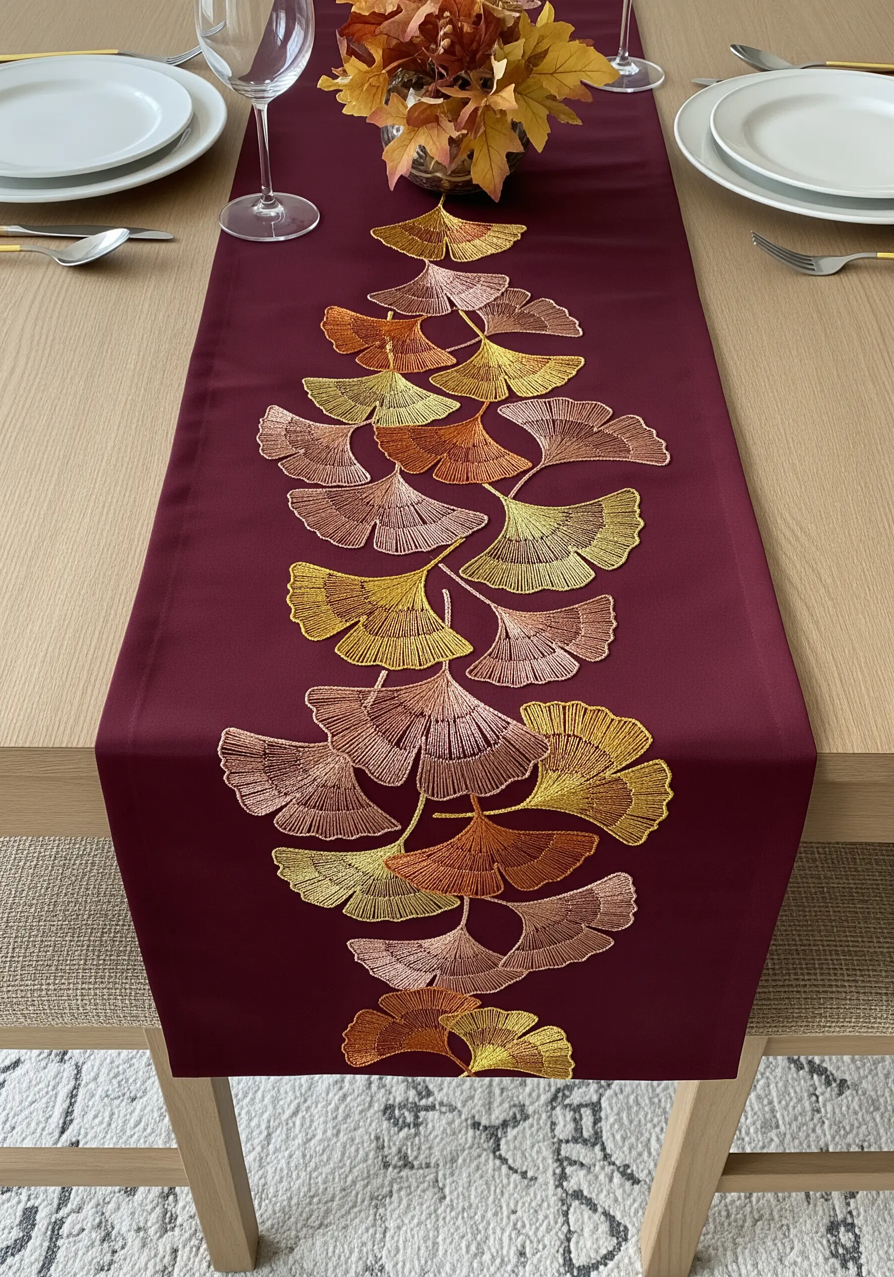 A burgundy table runner with a cascade of embroidered ginkgo leaves in blended metallic threads.