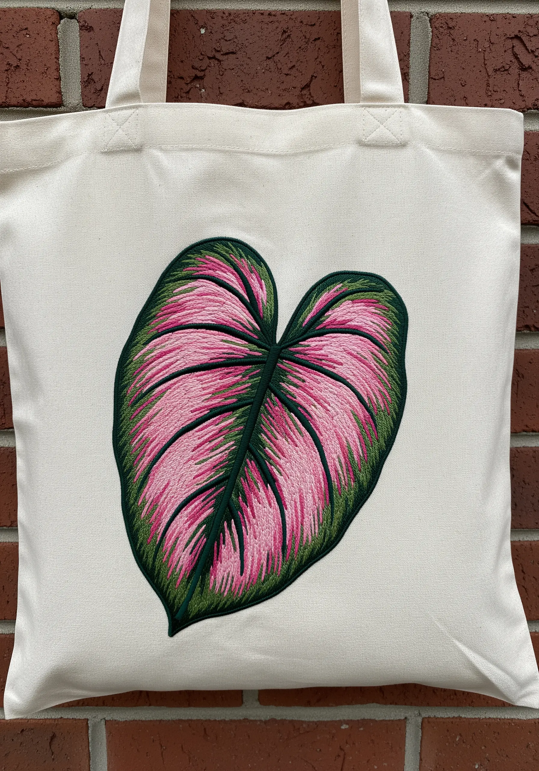 A large Pink Princess Philodendron leaf with blended pink and green threads on a tote bag.