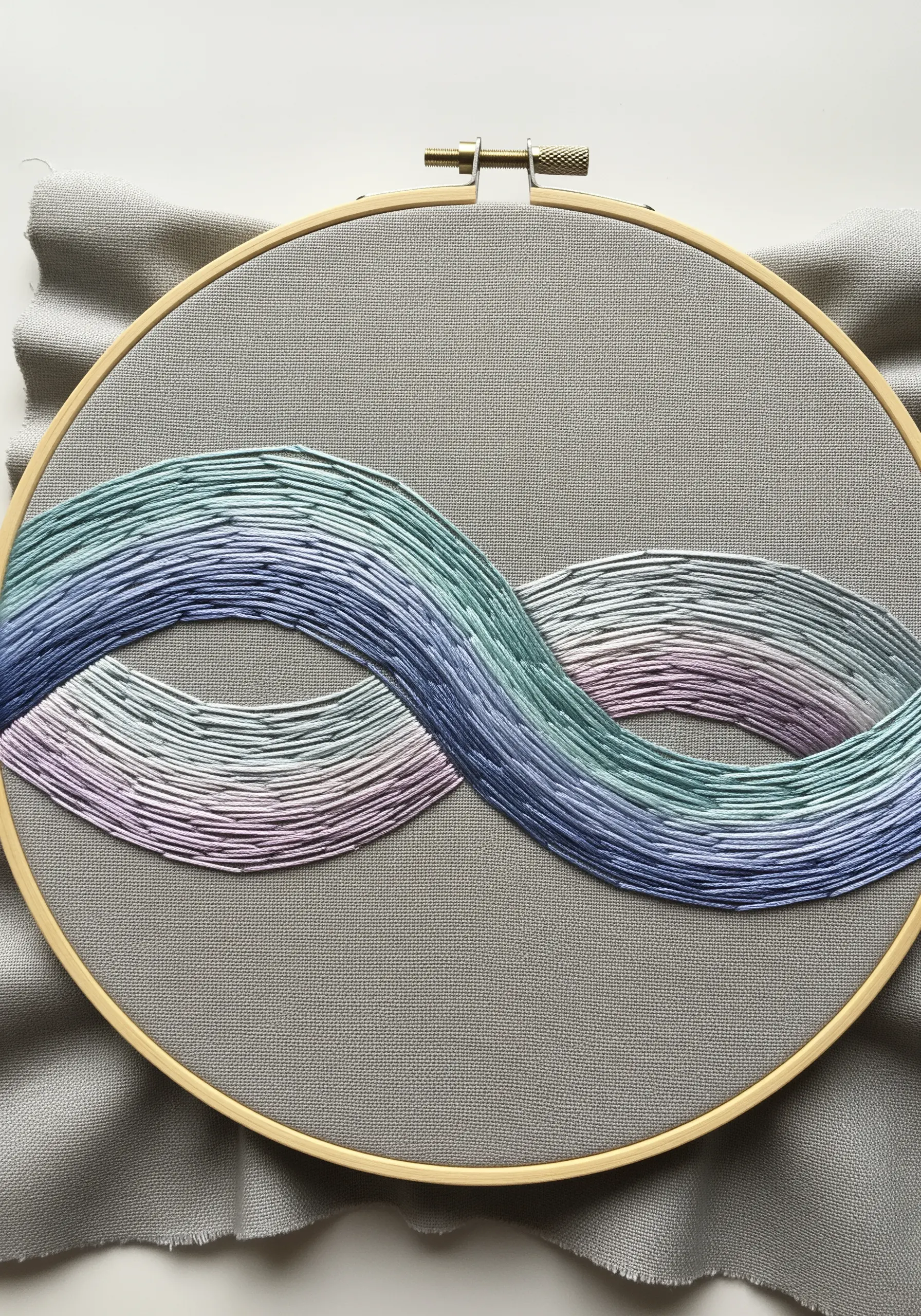 Abstract infinity symbol in hoop art using long-and-short stitch for a pastel color gradient.