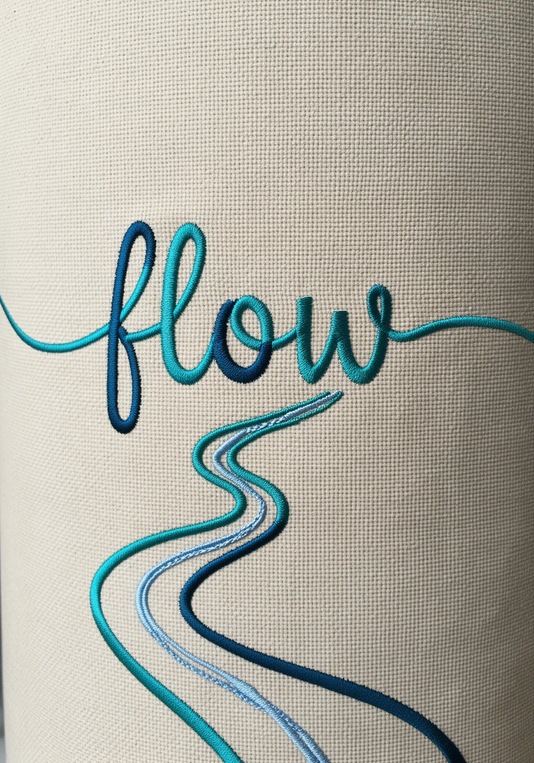 The word 'flow' embroidered in a gradient of blue and teal threads above flowing lines