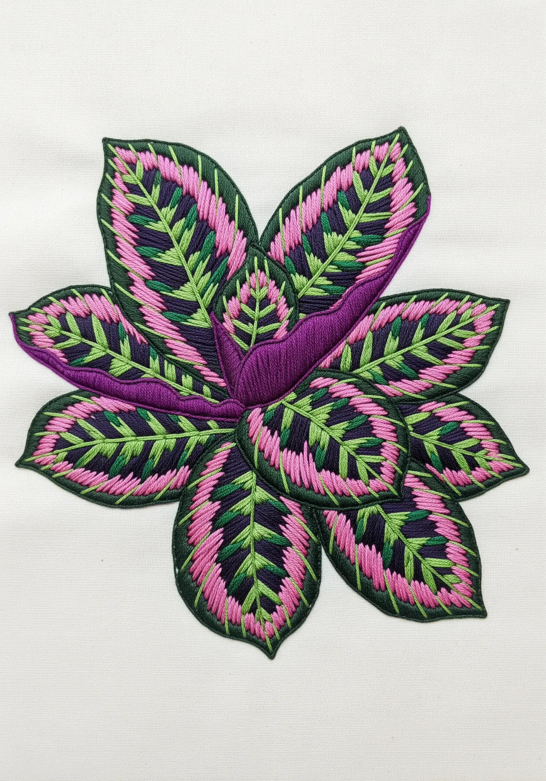 An embroidered Calathea plant with pink, green, and purple patterned leaves.