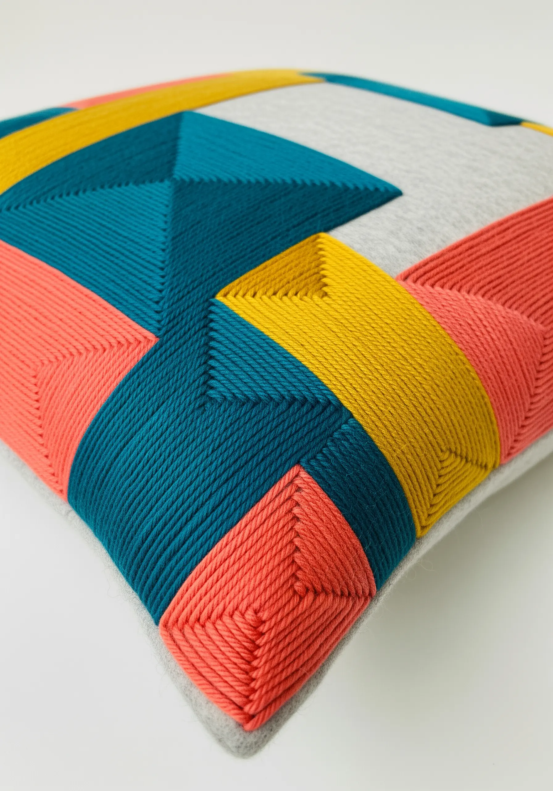 A close-up of a cushion with geometric blocks of color created with thick yarn