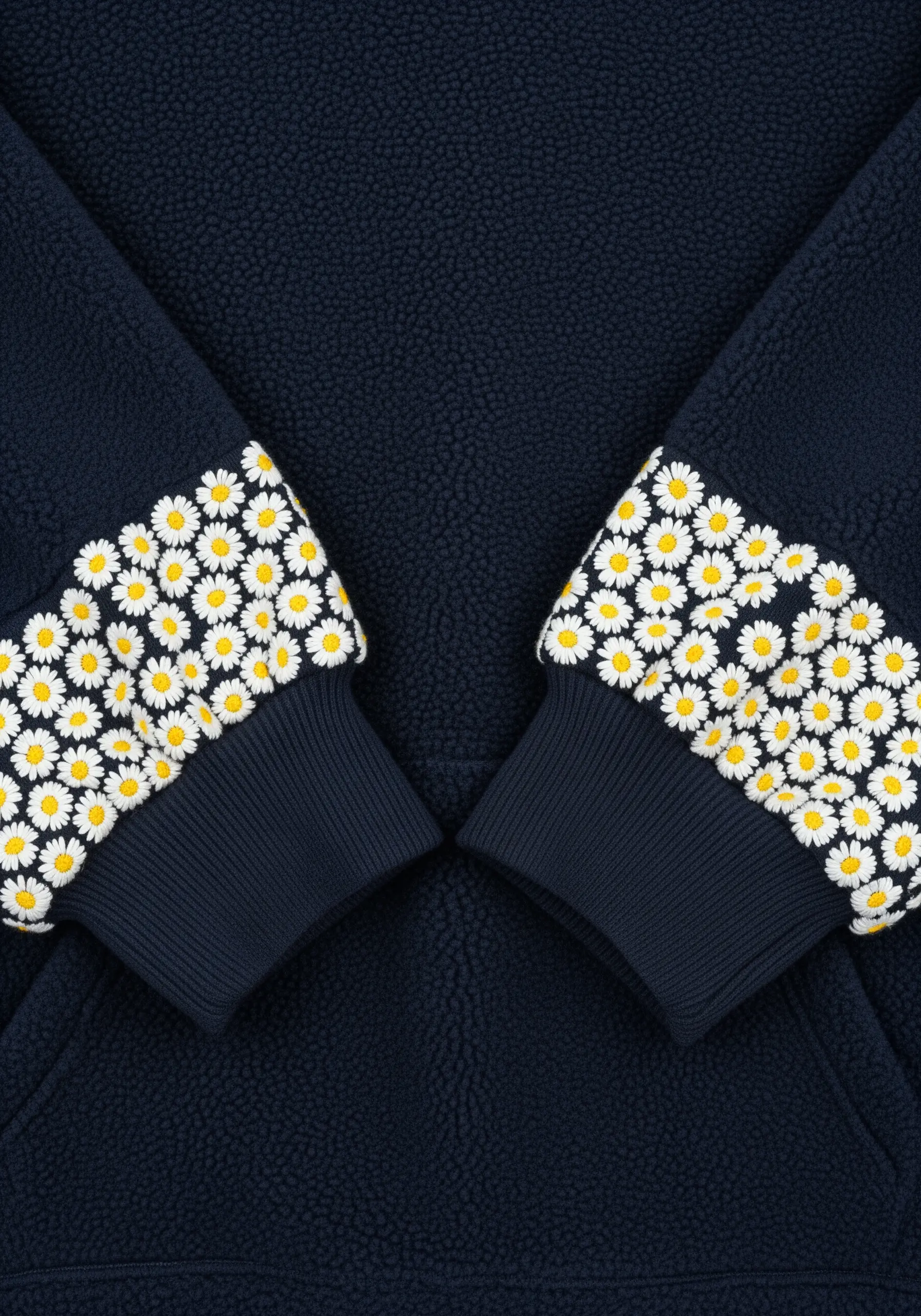 Dense bands of embroidered daisies around the cuffs of a navy blue fleece pullover.