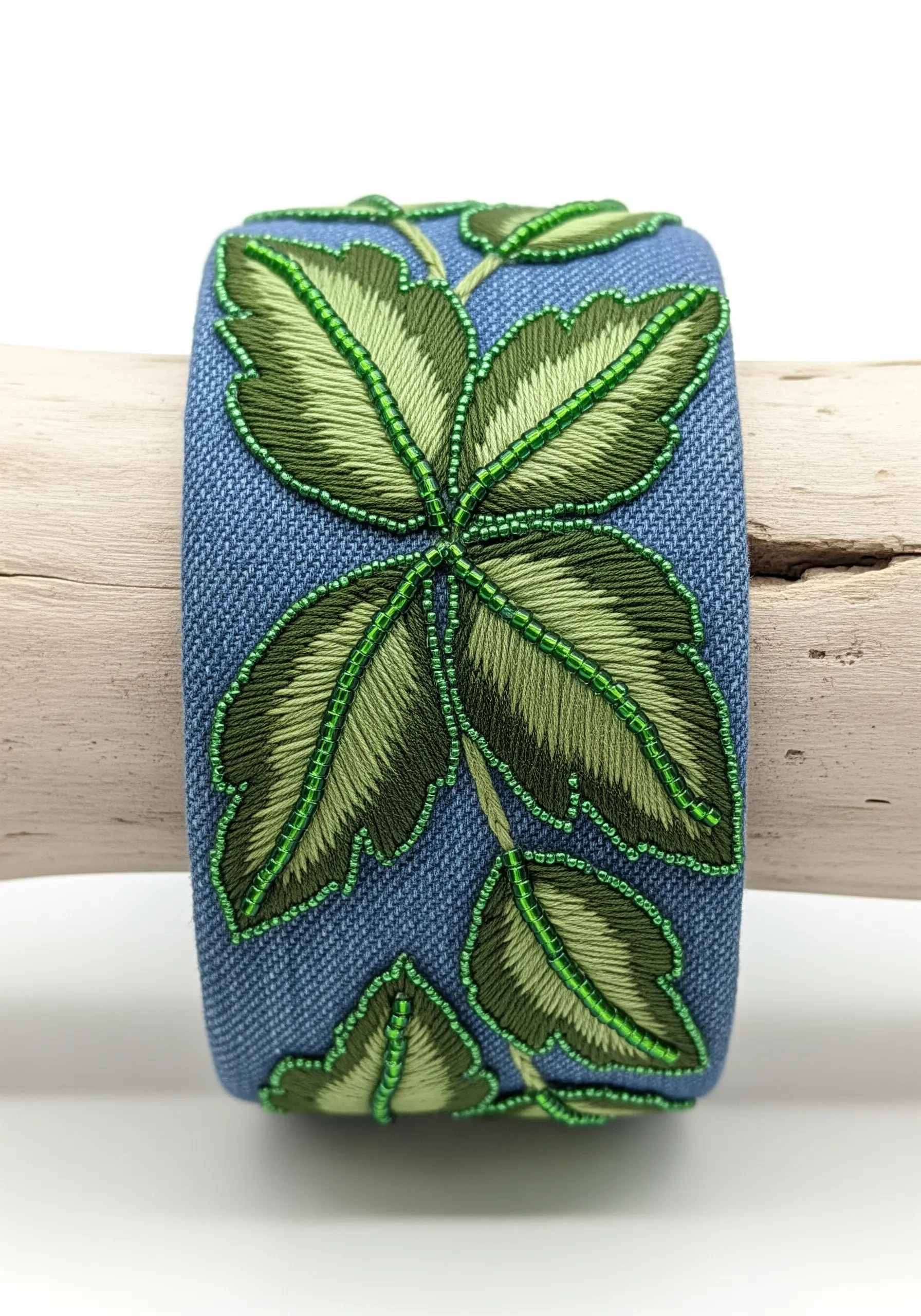 Embroidered cuff bracelet with green leaves outlined in matching green seed beads.