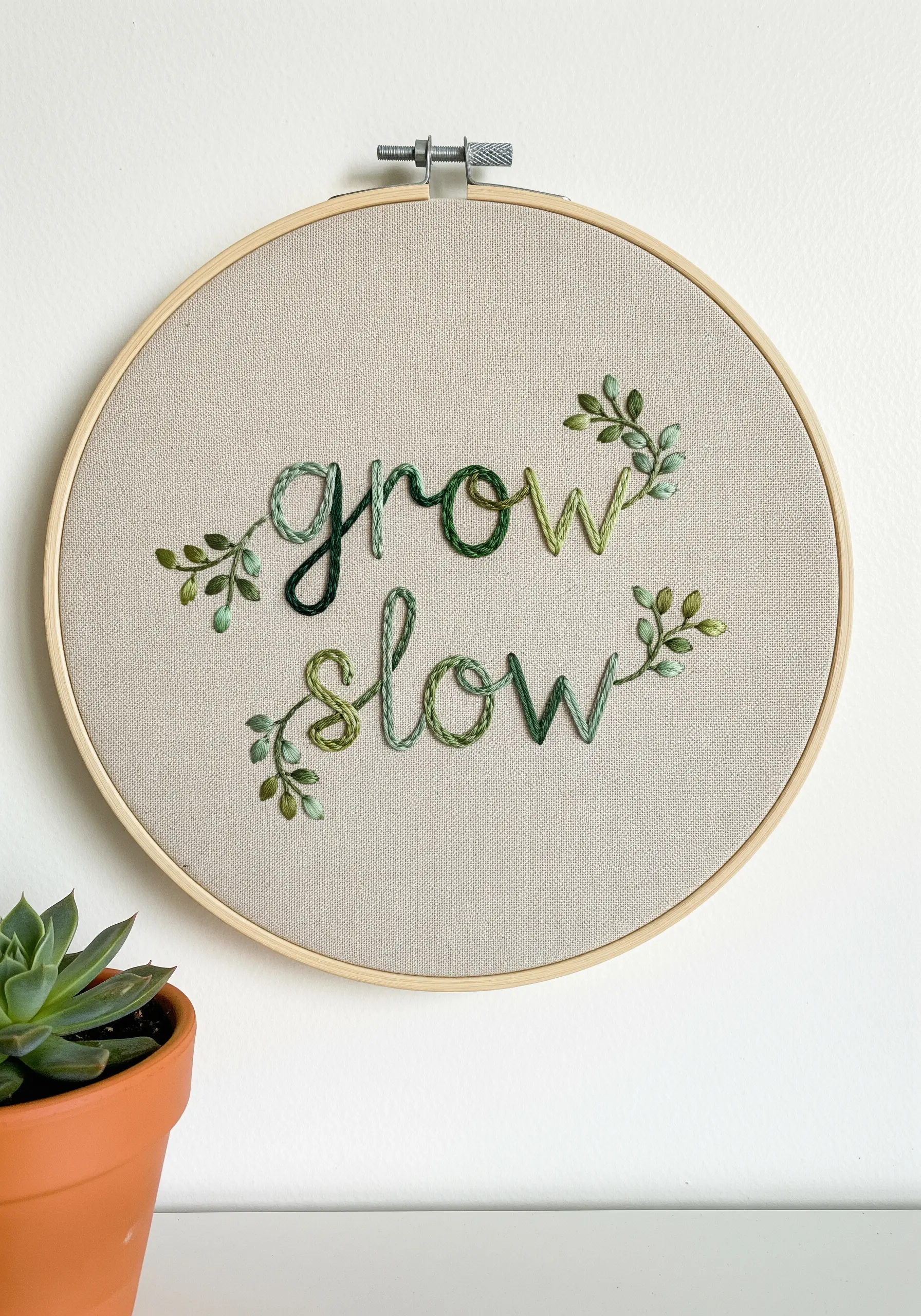 Cursive letters made of green variegated thread with small embroidered leaves.