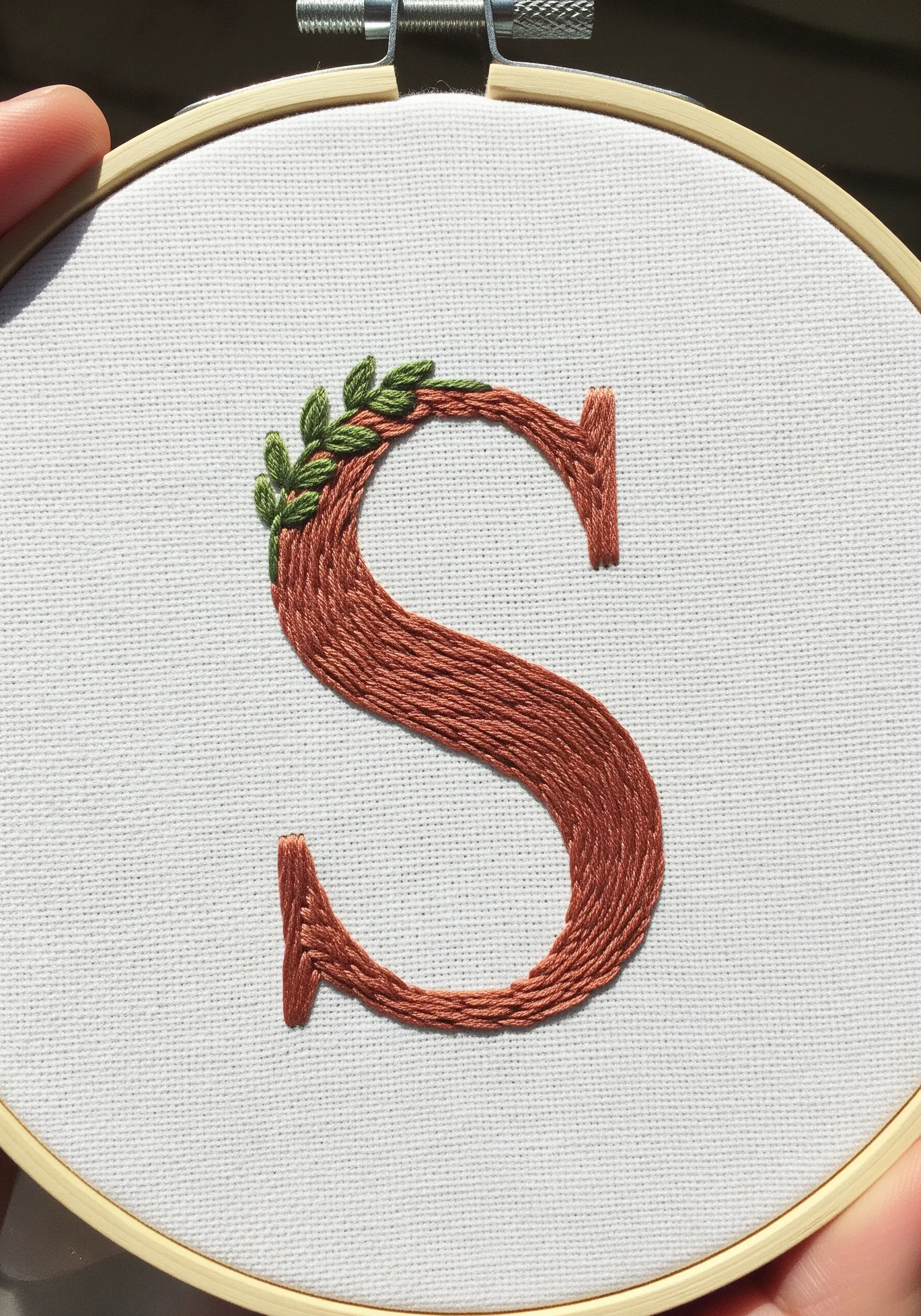 Satin stitch monogram letter 'S' with a small vine of fishbone stitch leaves.