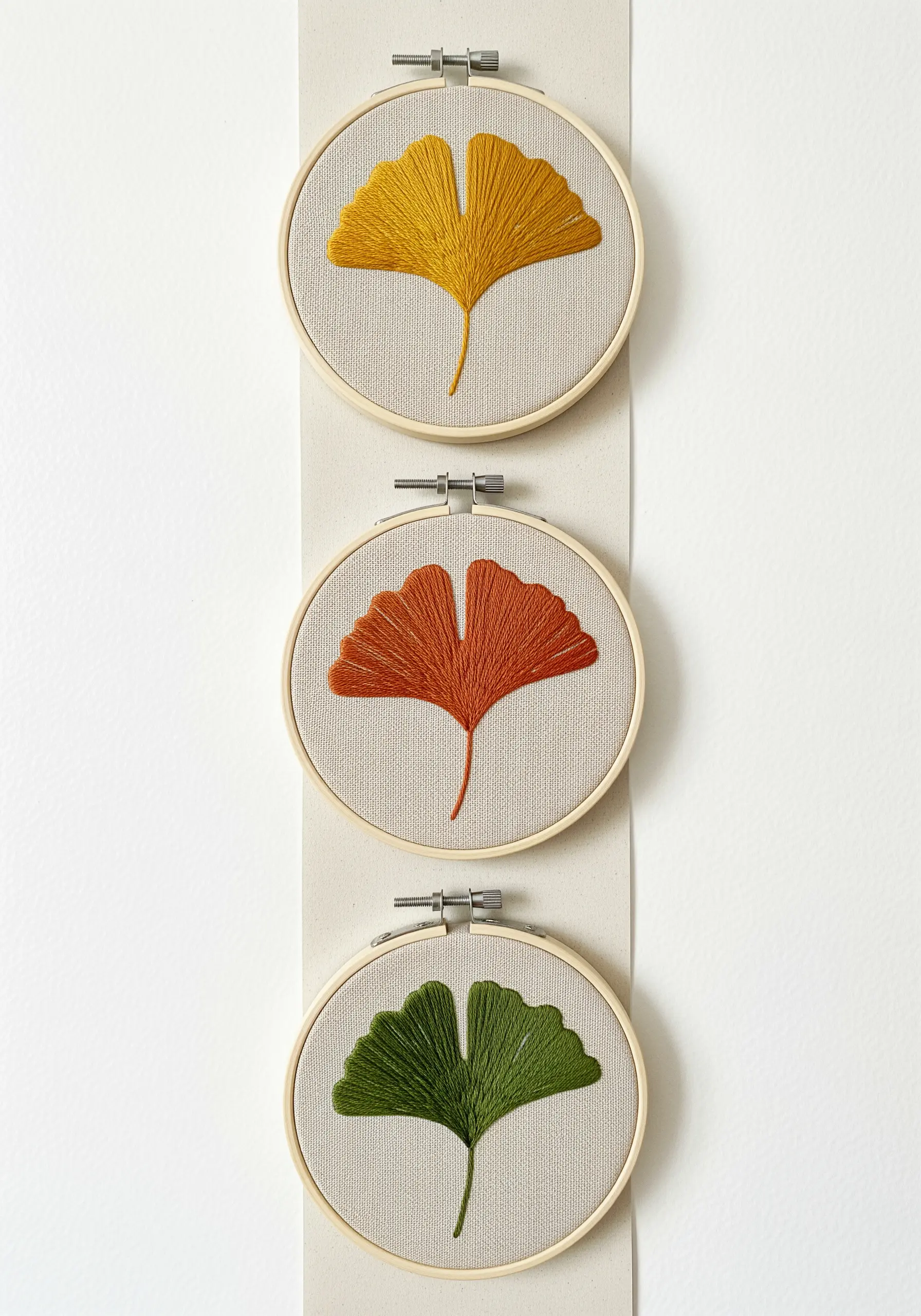 Three embroidery hoops with ginkgo leaves in yellow, orange, and green satin stitch.