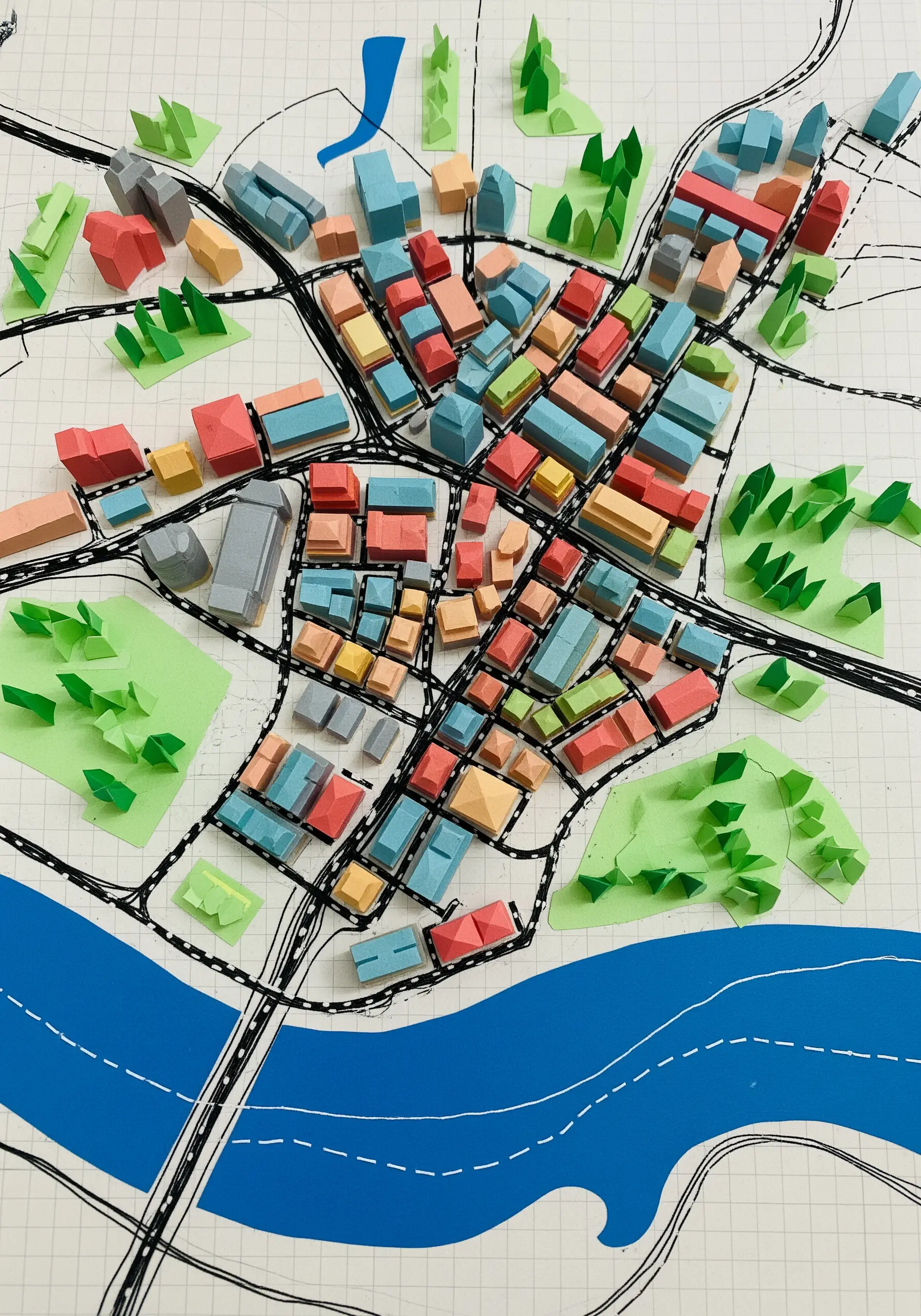 A 3D city map made with colorful folded paper buildings on a hand-drawn grid.