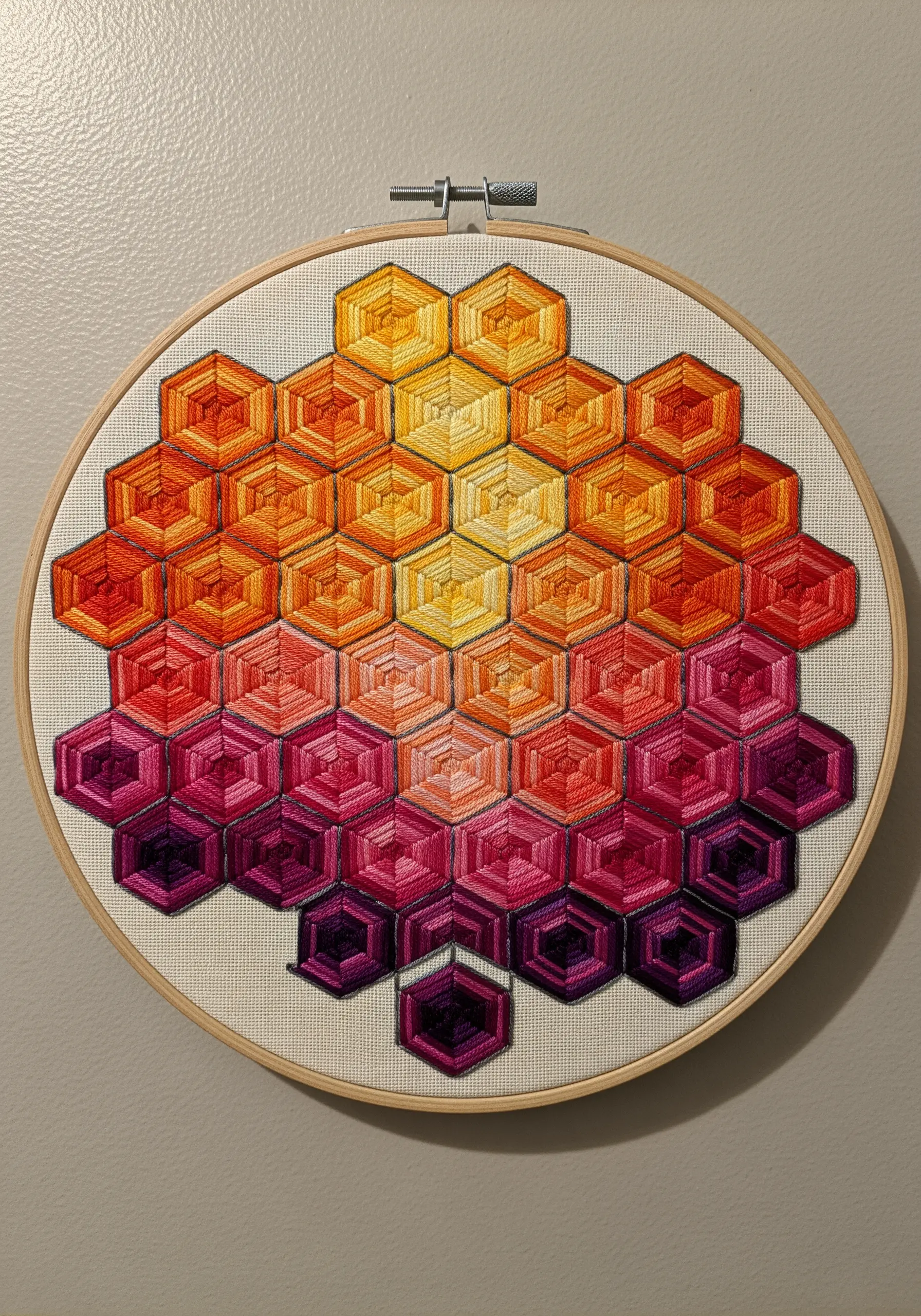 A geometric pattern of stitched hexagons in a warm sunset gradient of yellow, orange, and purple.