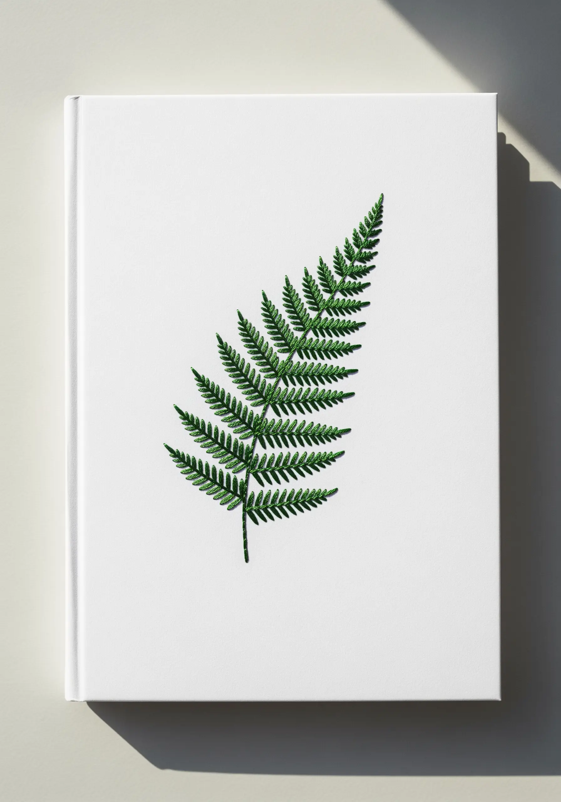 A detailed green fern embroidered on a white notebook cover, showing precise leaflets.