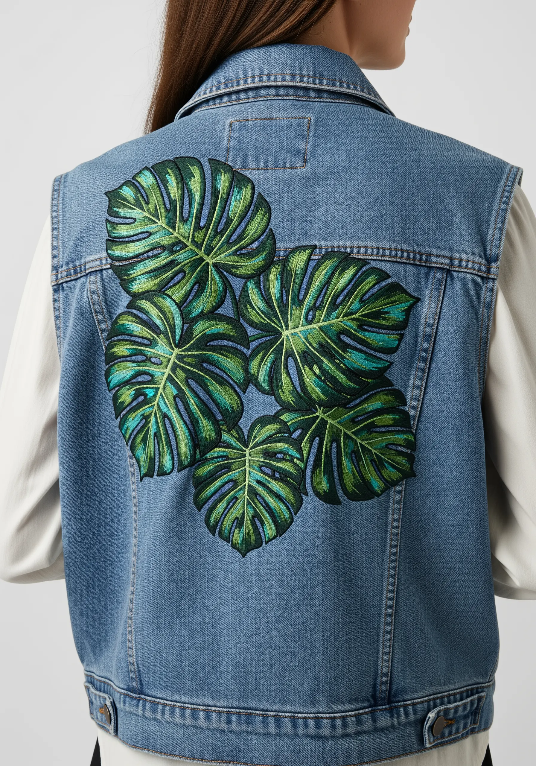A cluster of overlapping monstera leaves in various shades of green on a denim vest.