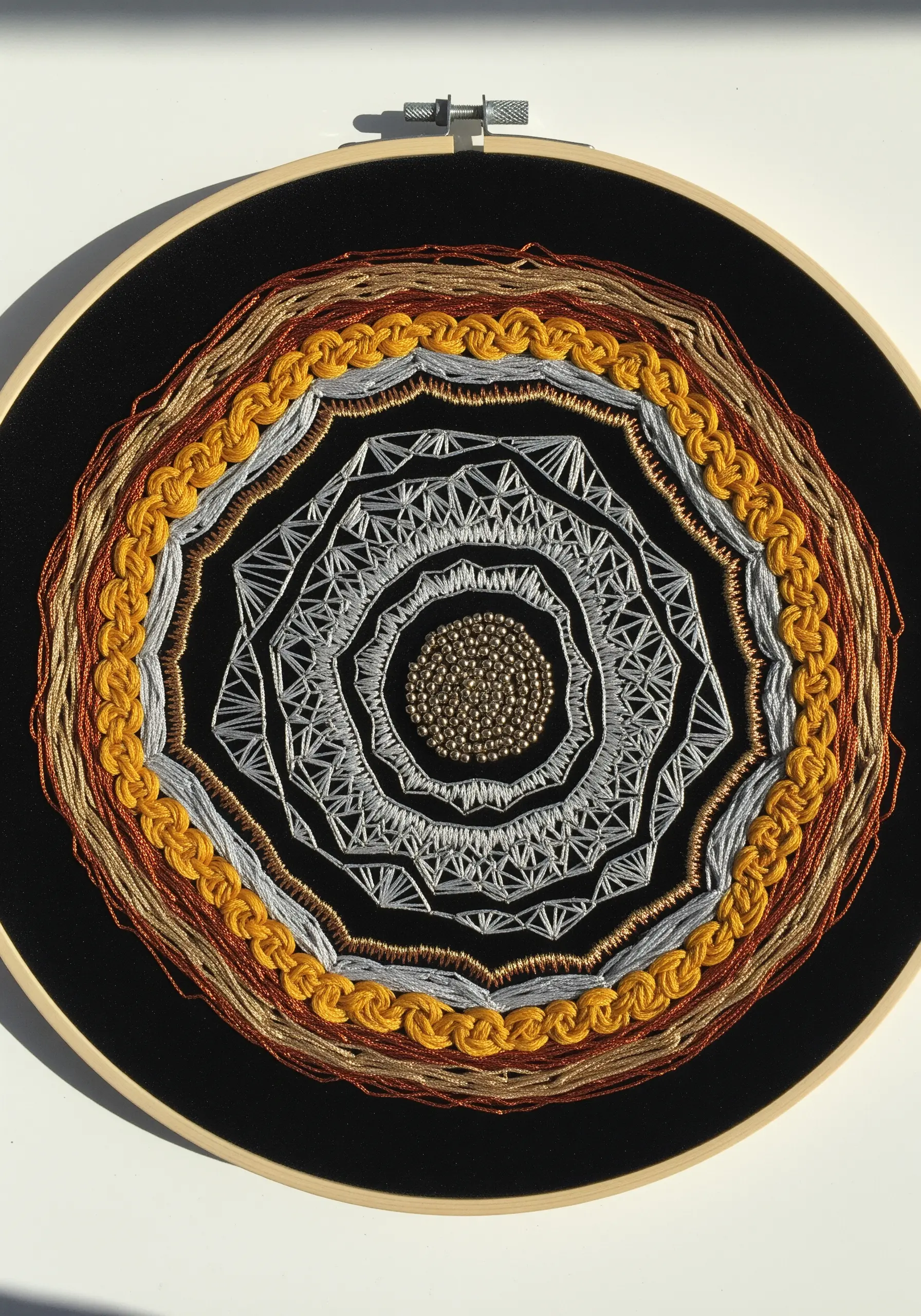 Abstract mandala hoop with layered gold, silver, and copper metallic threads on black fabric.
