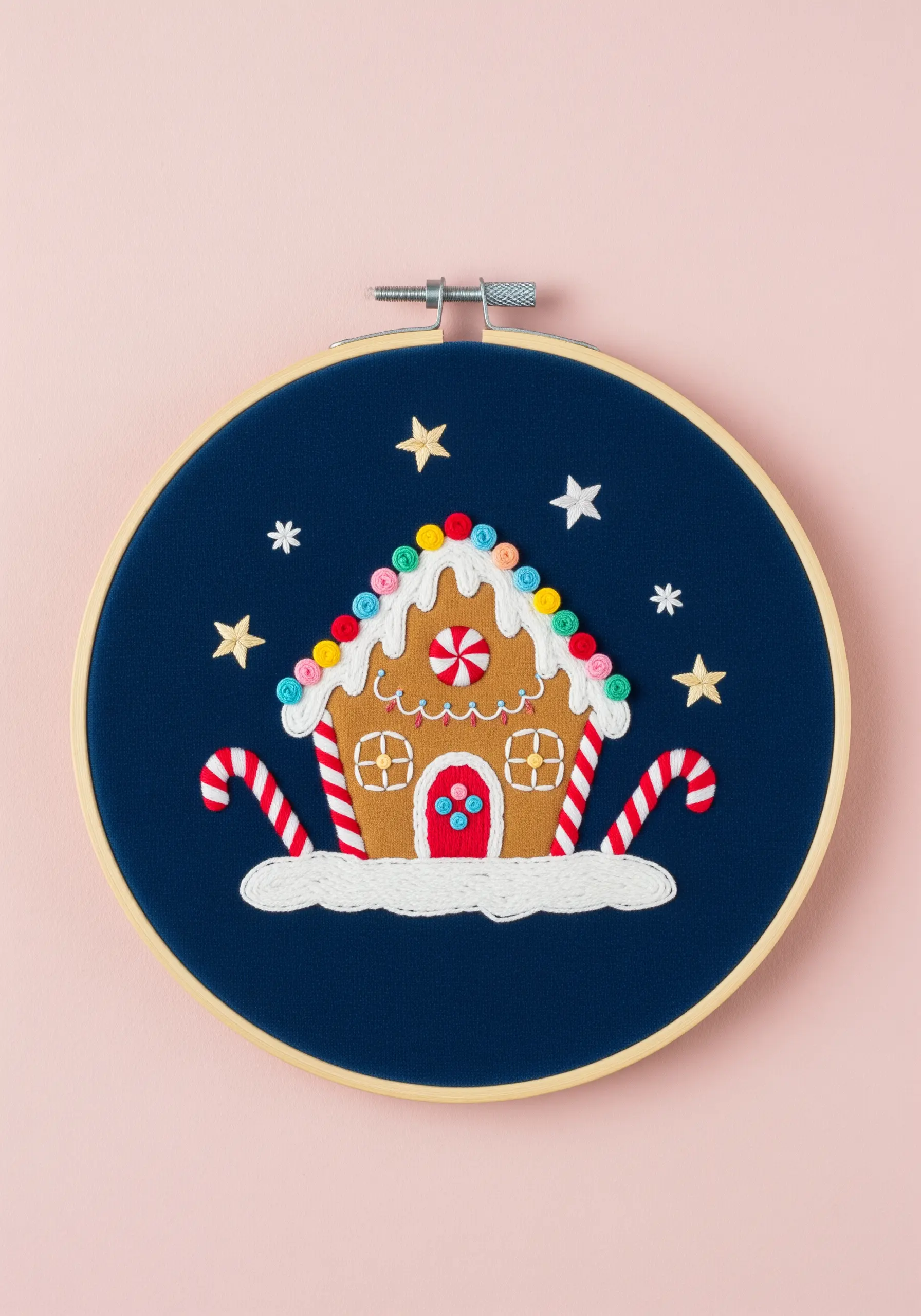 A whimsical gingerbread house embroidery with colorful French knot gumdrops and striped candy canes.