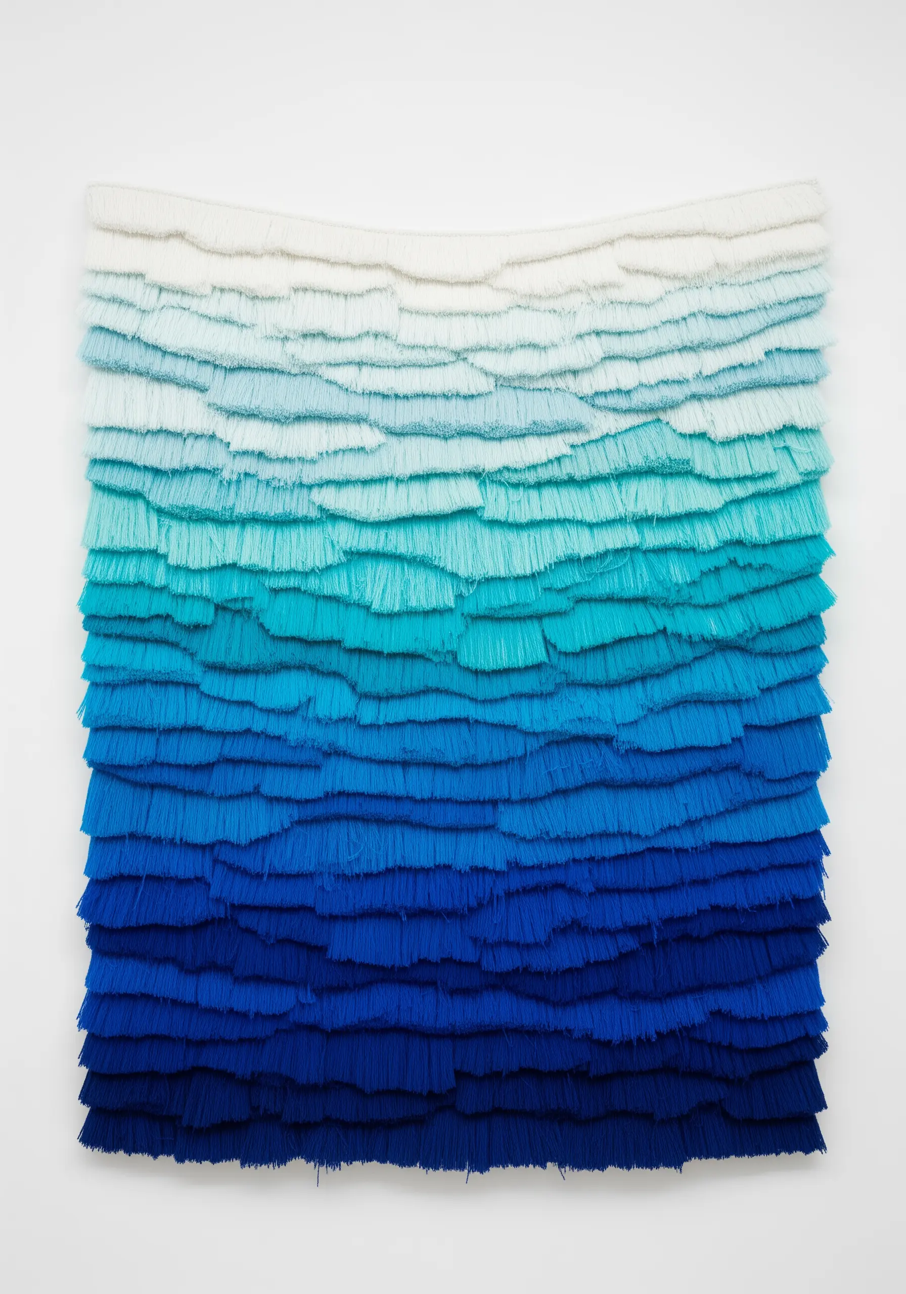 A wall hanging with dense, trimmed fringe in a blue gradient, from white to deep royal blue