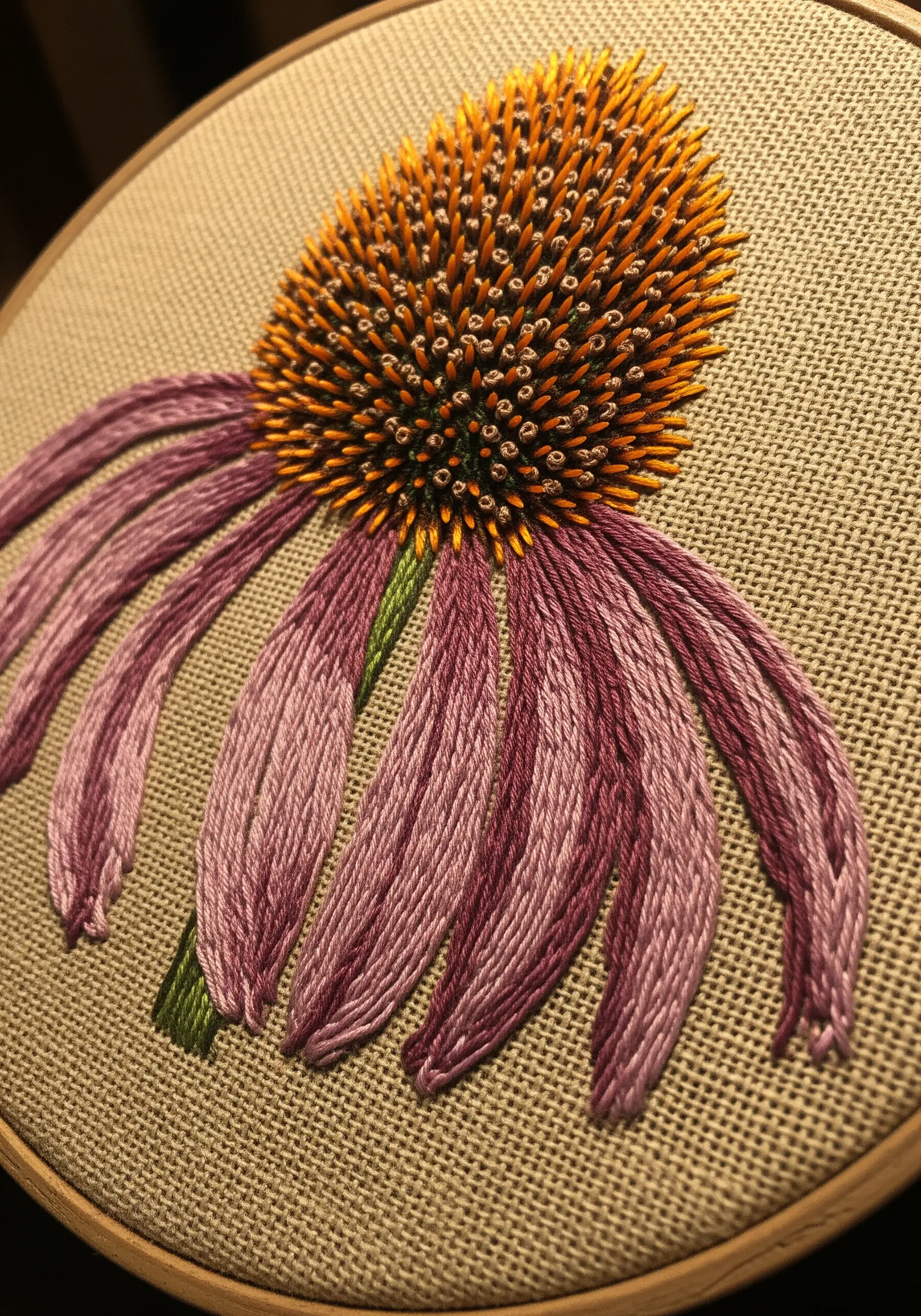 A close-up of an embroidered coneflower with a highly textural, spiky center and purple petals.