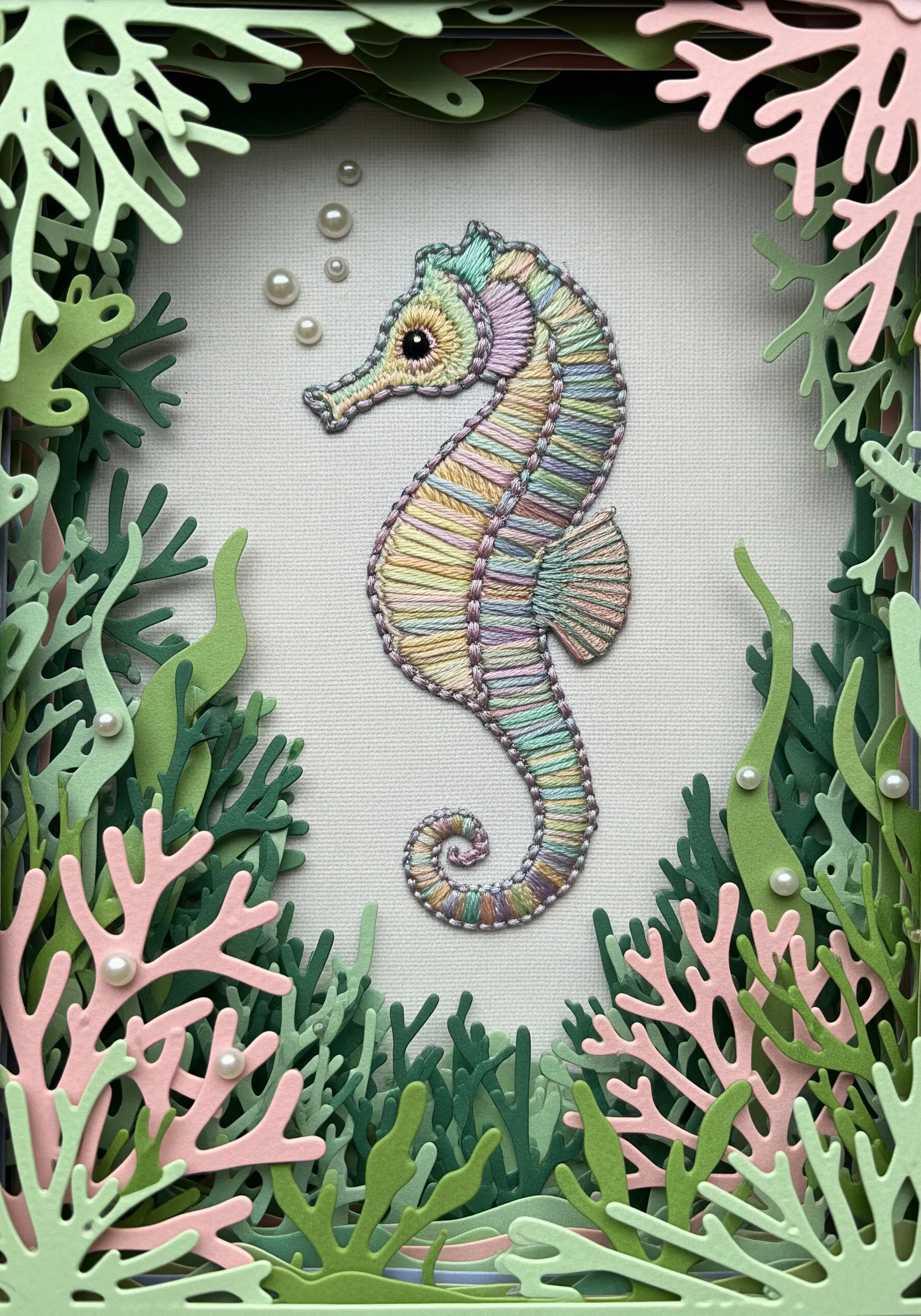 Embroidered seahorse in a hoop, framed in a shadowbox with layered paper-cut seaweed.