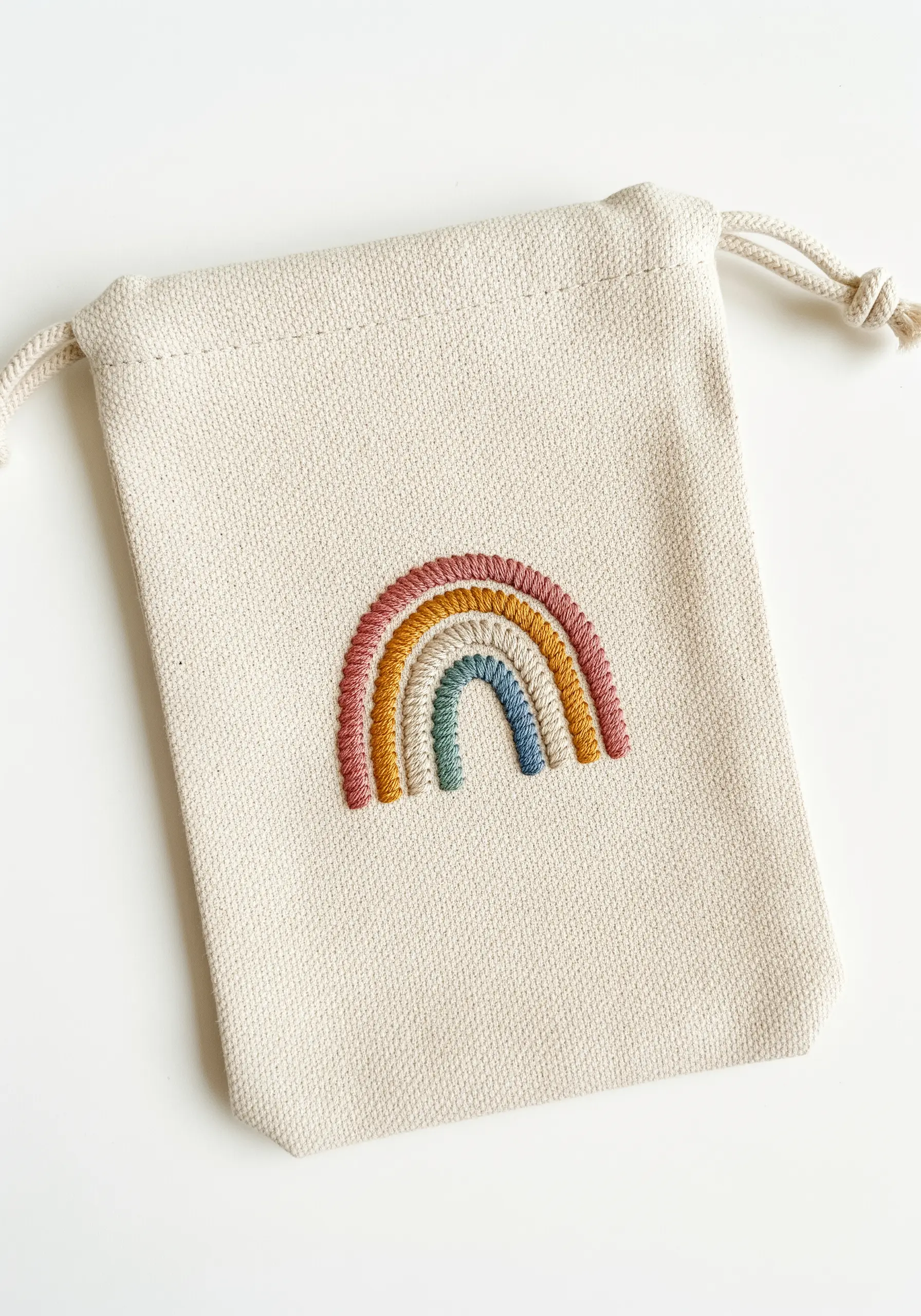 A small, textured rainbow with five earthy colors embroidered on a drawstring pouch.