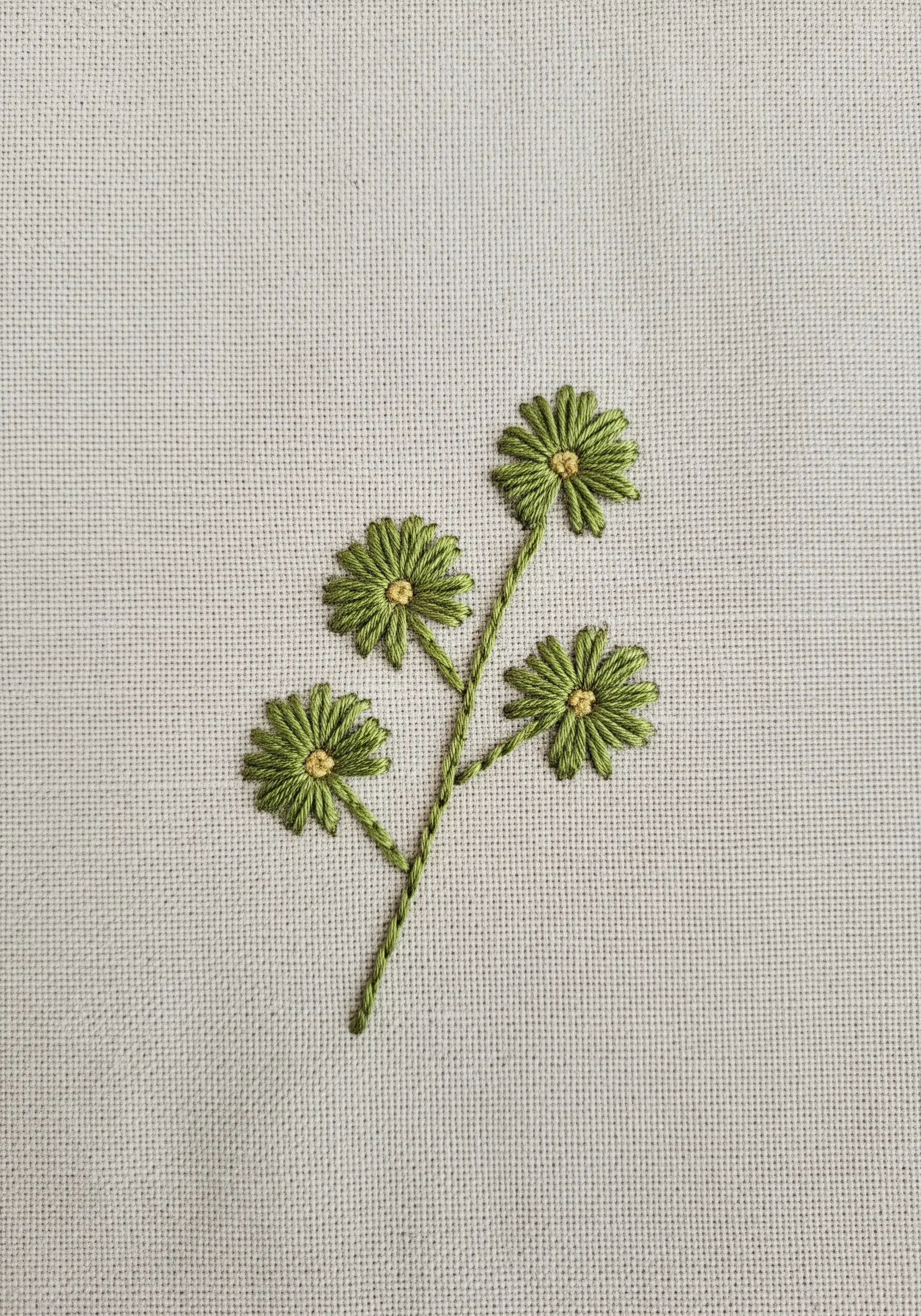 Four small green daisies made with lazy daisy stitches on neutral linen.
