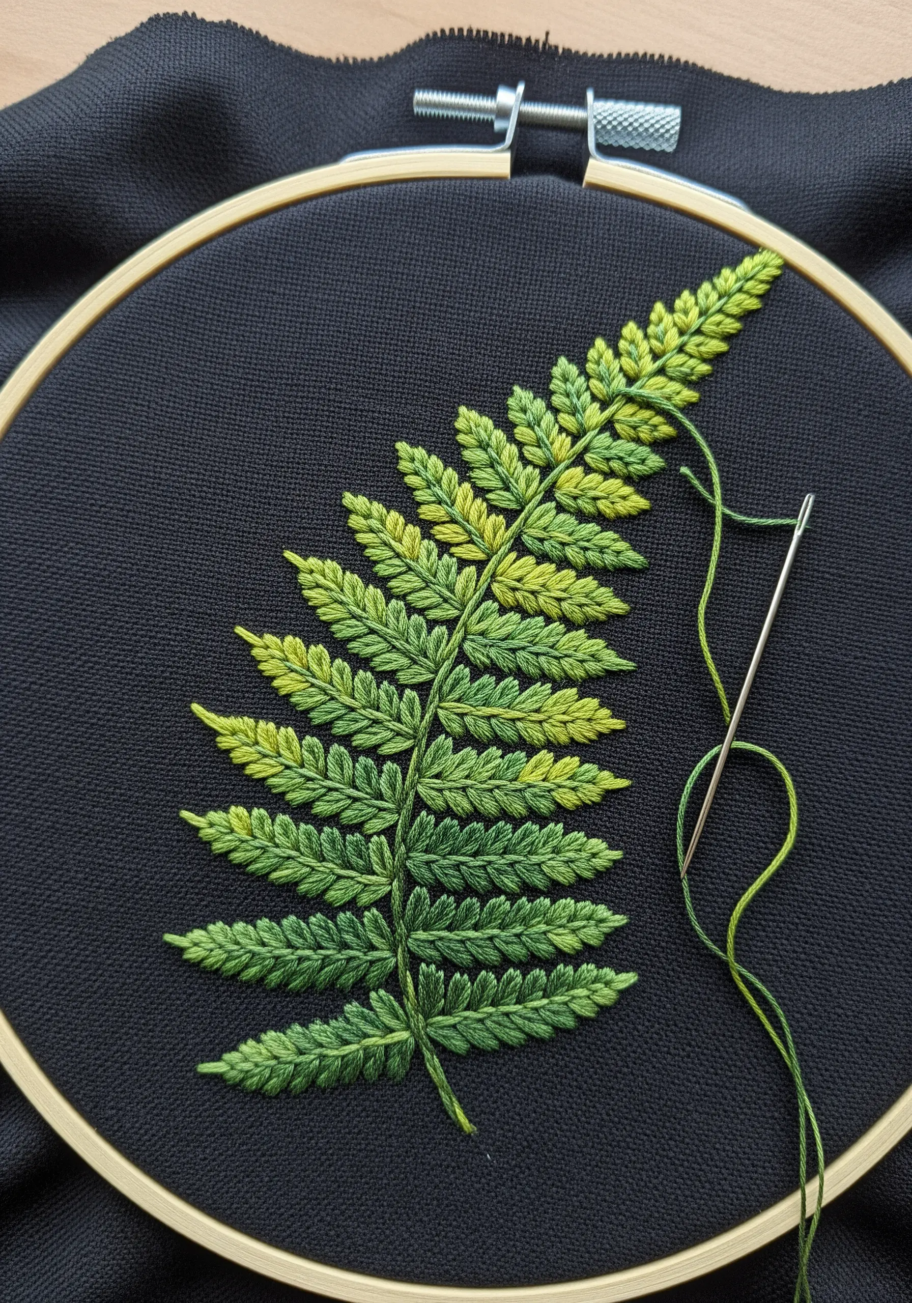 Close-up of a fern leaf embroidered in shades of green on black fabric.