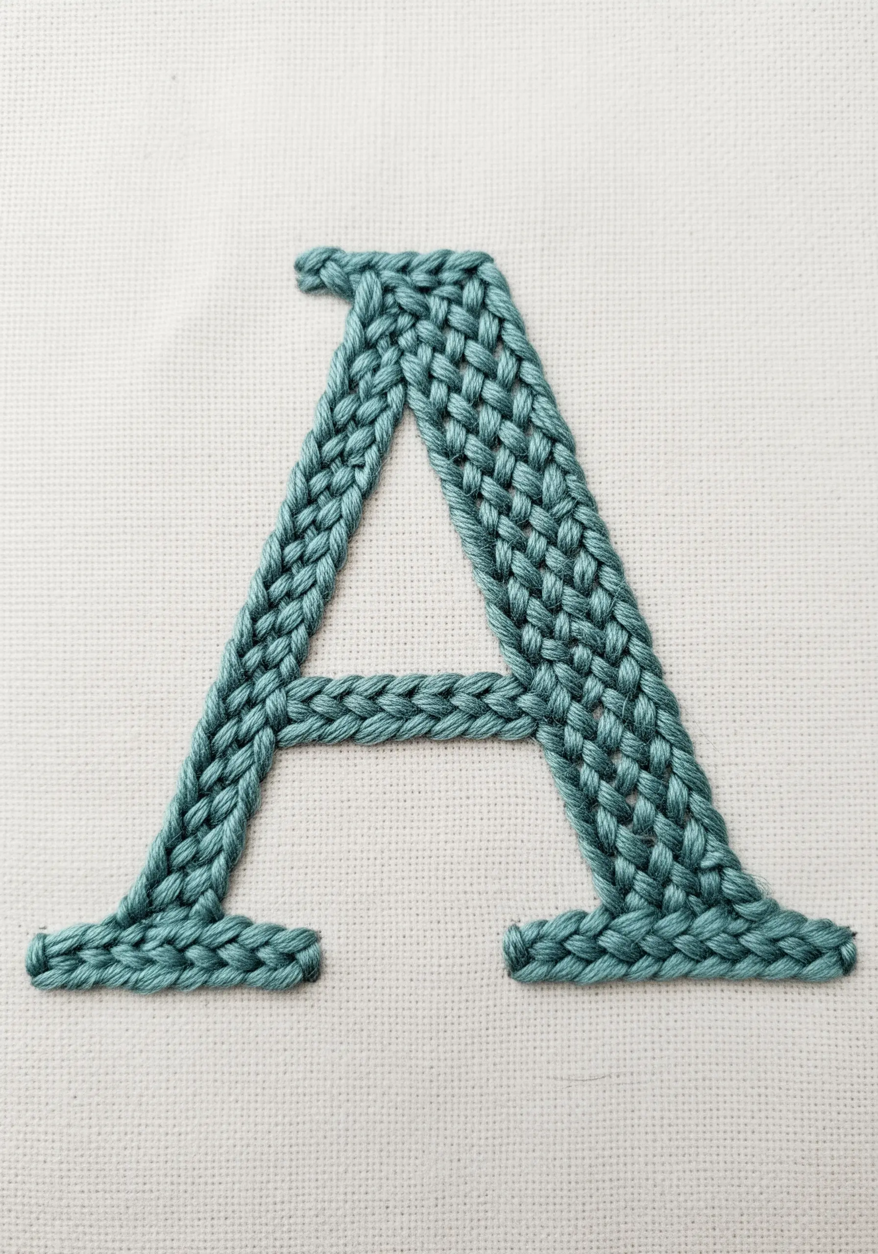 The letter 'A' embroidered with a dimensional, braided teal stitch on white fabric.