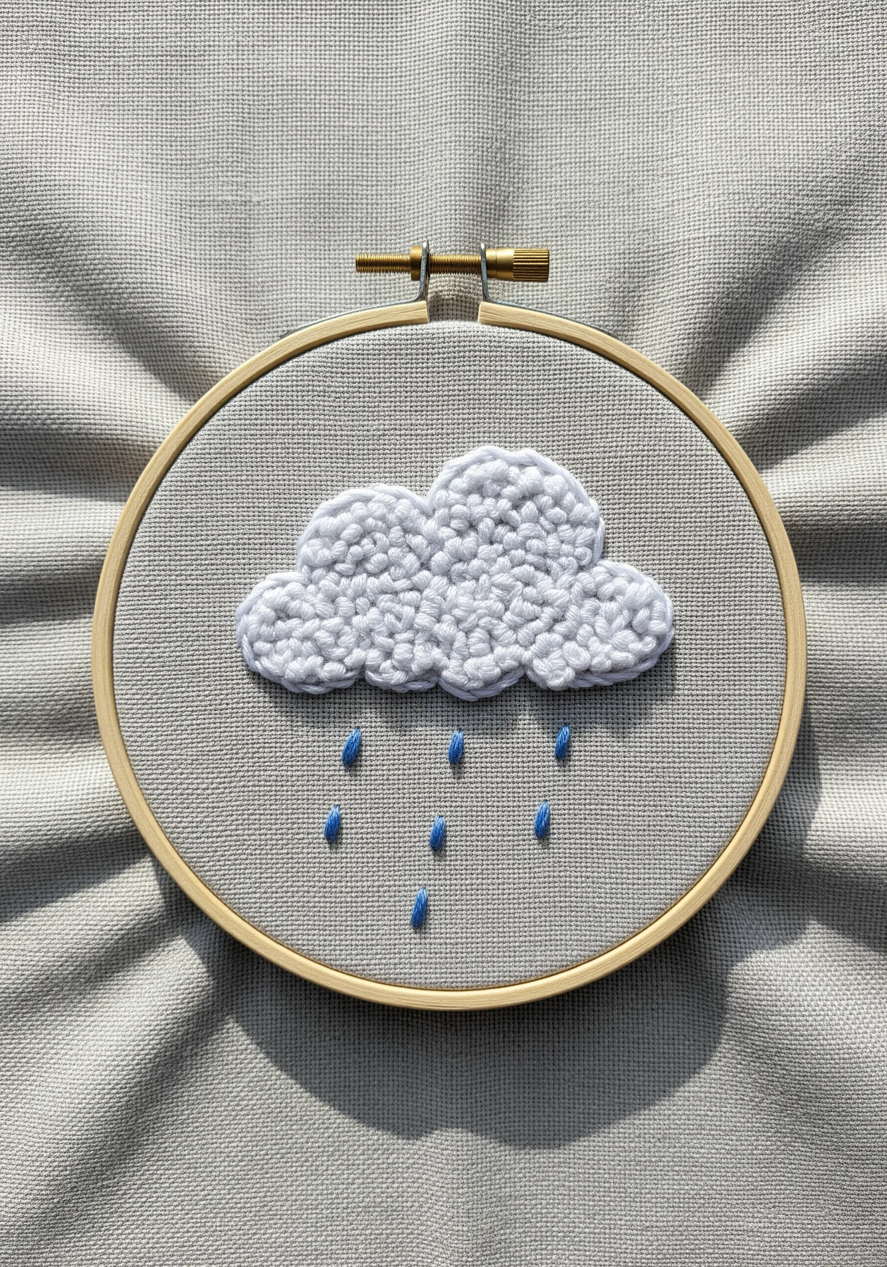 A puffy white cloud made of French knots with blue raindrops.