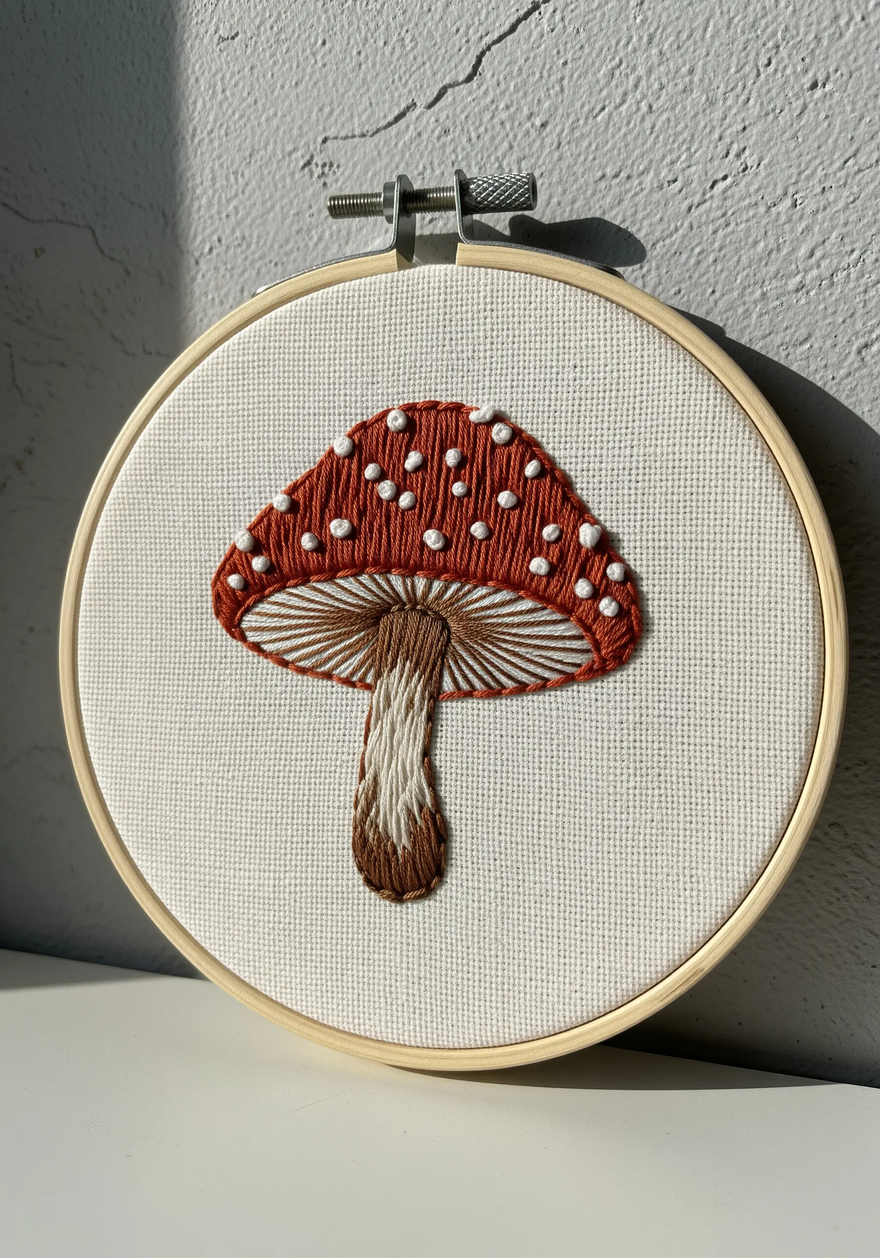 Red mushroom with white French knot spots and straight-stitched gills in an embroidery hoop.