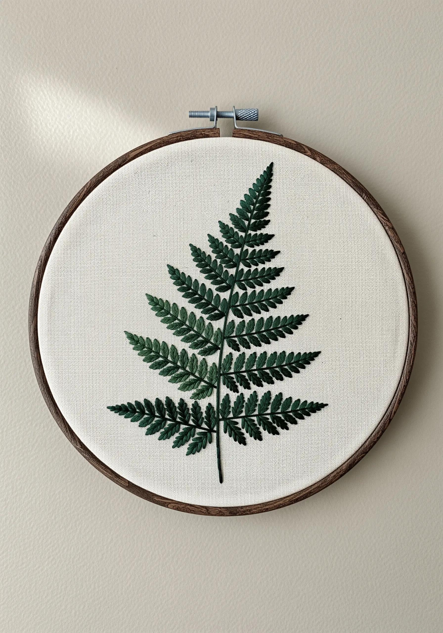 Realistic fern leaf embroidery using shades of green on off-white fabric in a dark hoop.