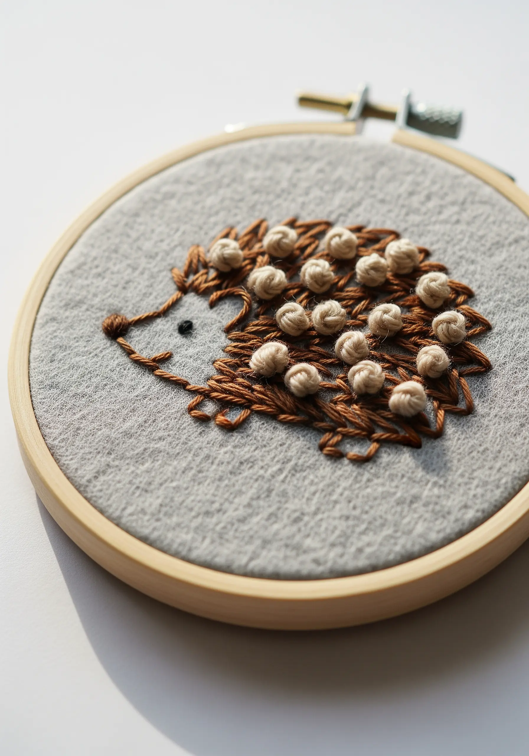 Embroidered hedgehog with a textured back made of French knots on grey felt.
