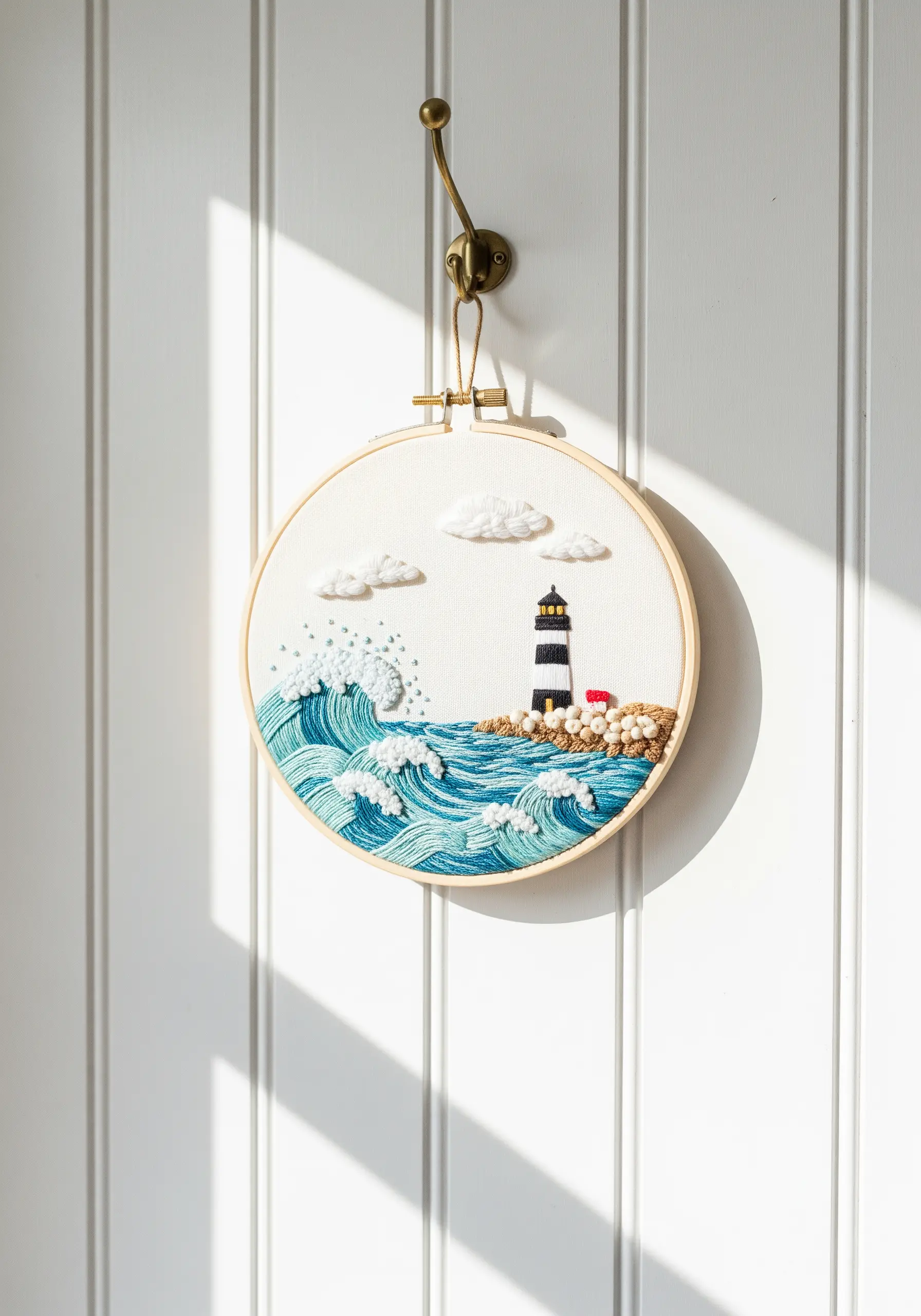 Embroidery hoop art of a lighthouse scene with highly textured waves and clouds.