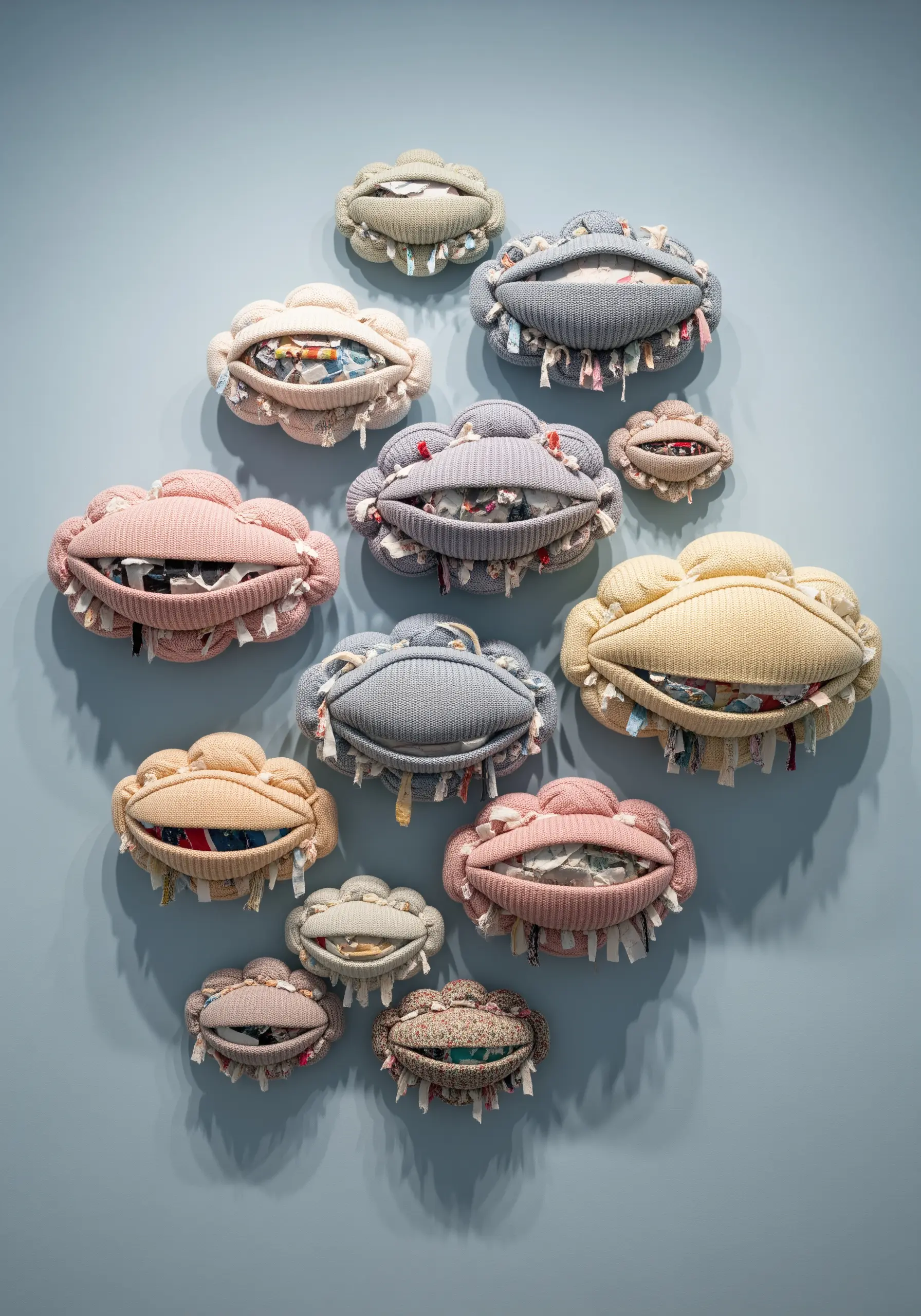 A collection of cloud-shaped soft sculptures in muted colors, made from knit fabric and stuffed with scraps.