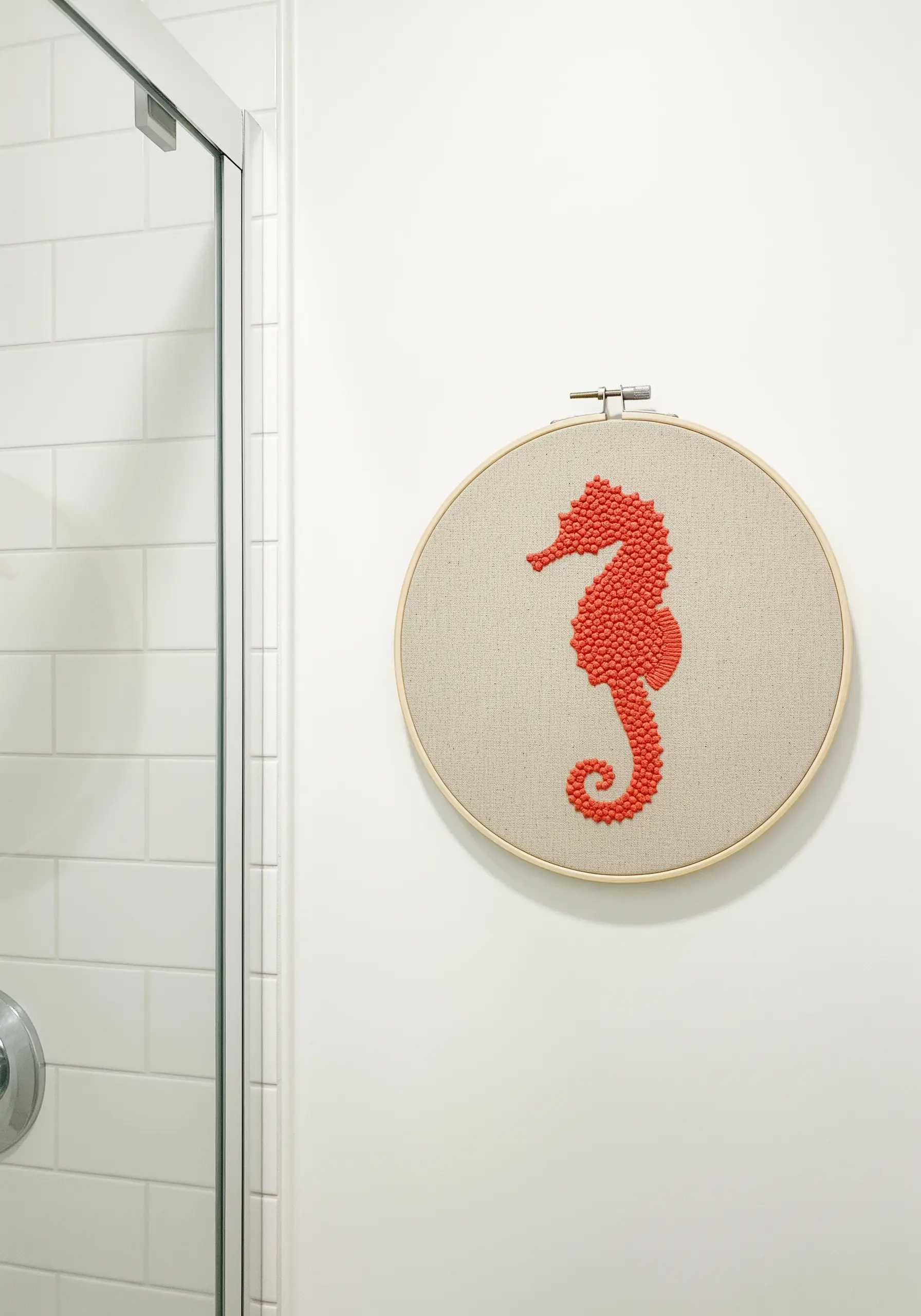 A seahorse silhouette filled entirely with vibrant coral-colored French knots on linen fabric.