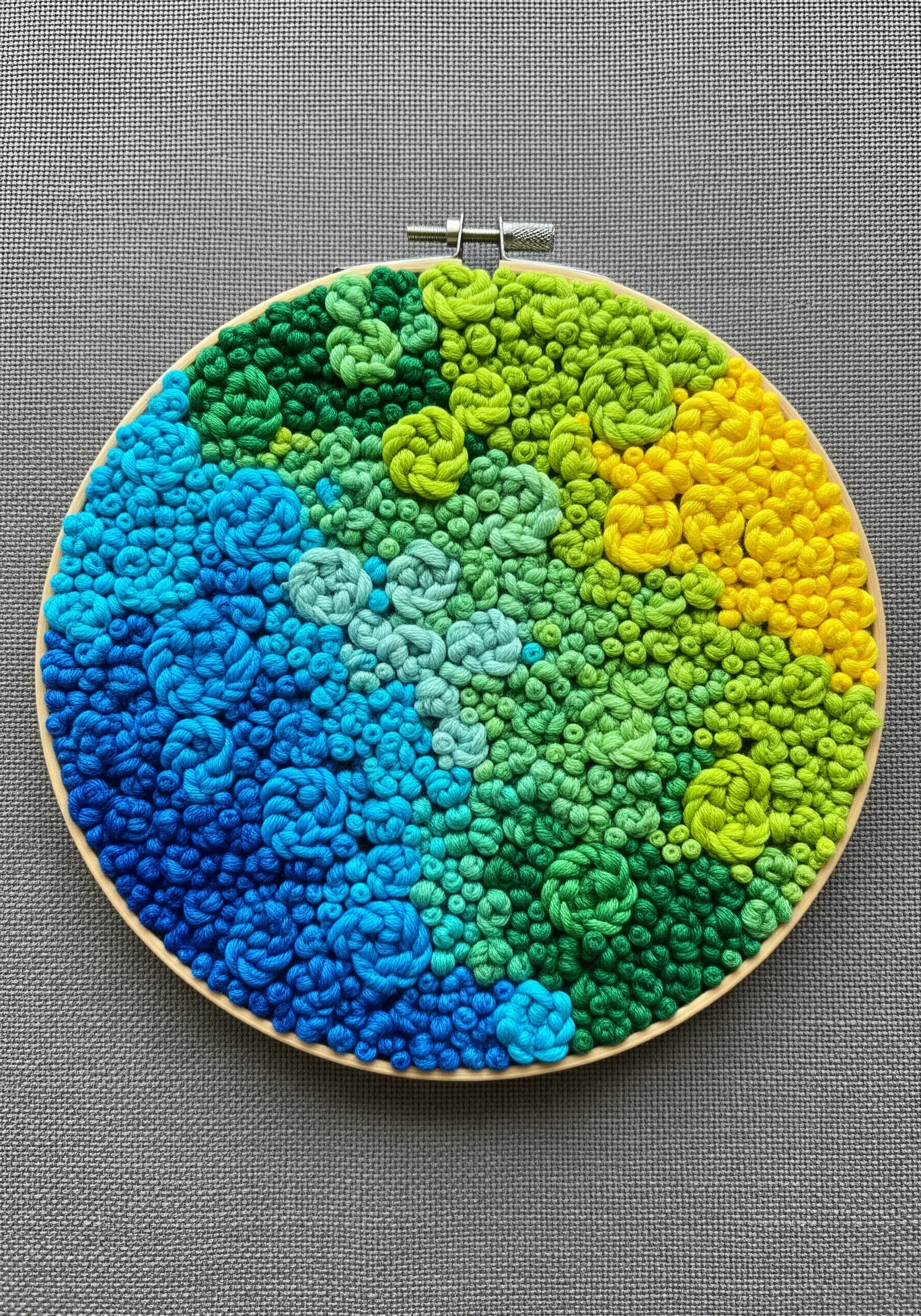 Embroidery hoop filled with a dense texture of blue, green, and yellow French knots.