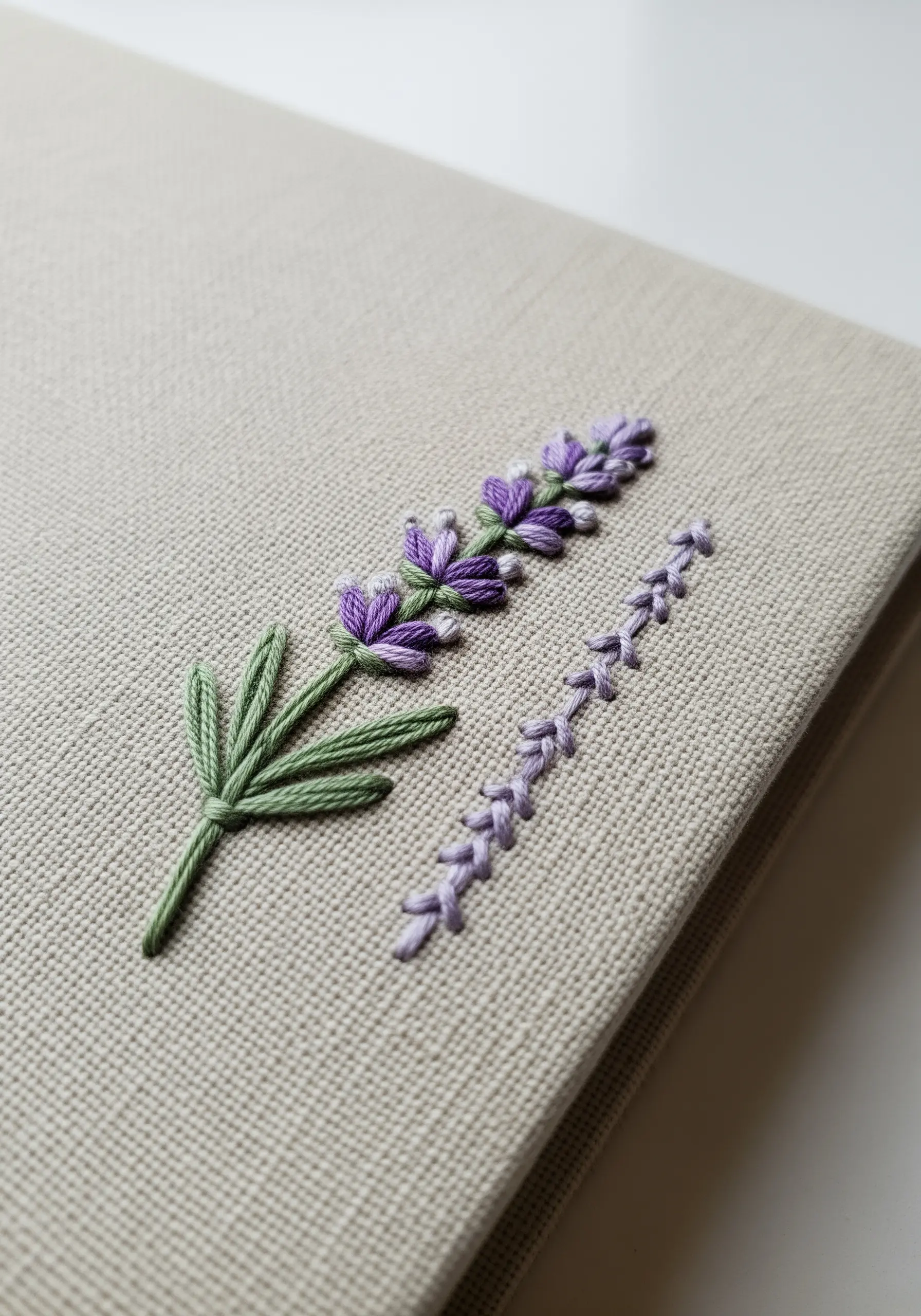Embroidered lavender sprig on a beige fabric notebook cover, showing texture.