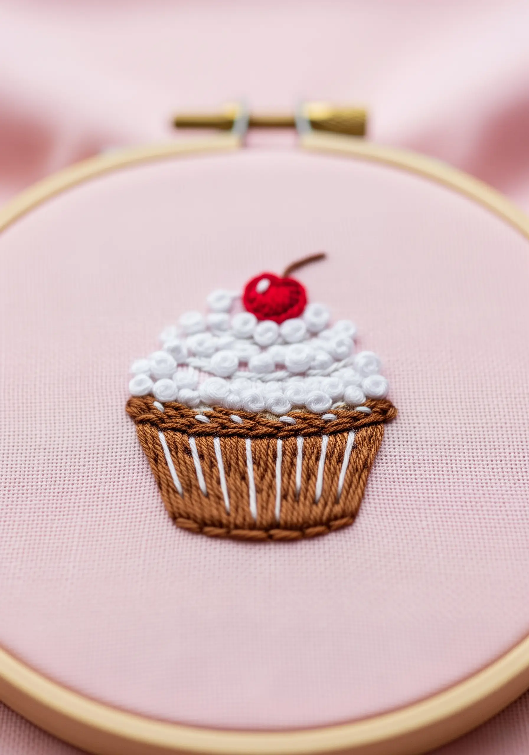 A mini embroidered cupcake with white French knot frosting and a red cherry.