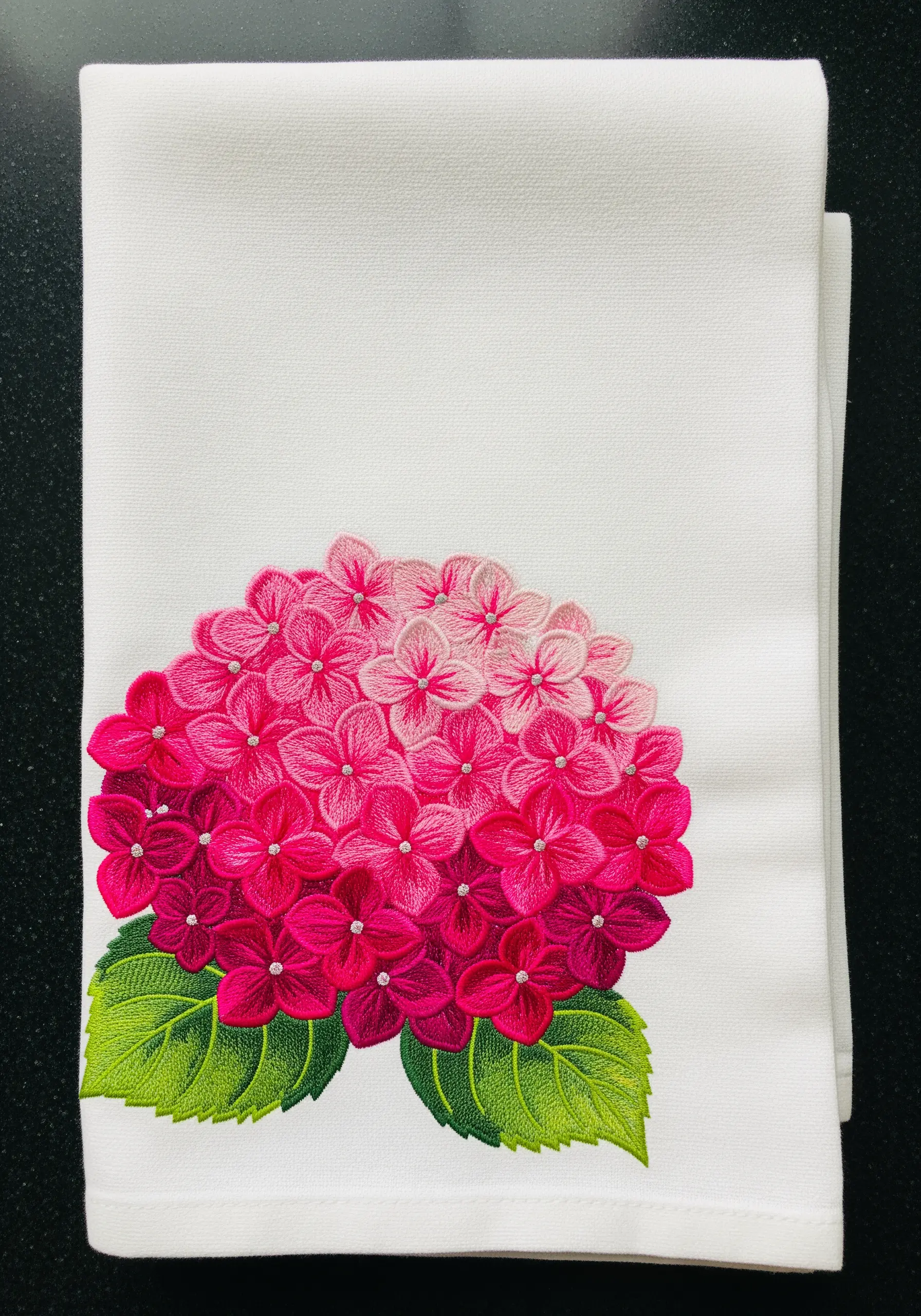 Vibrantly embroidered hydrangea on a white towel, blending from light pink to deep magenta.