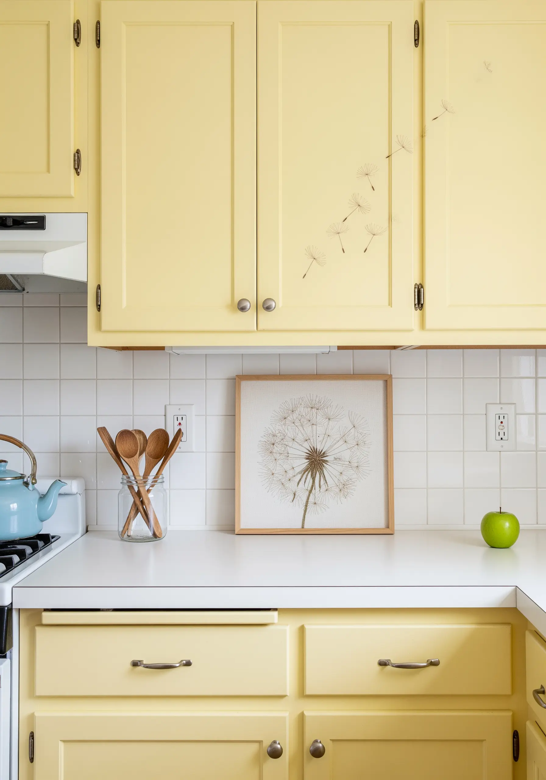 Framed embroidery of a dandelion head, with stitched seeds appearing to float up the kitchen cabinets.