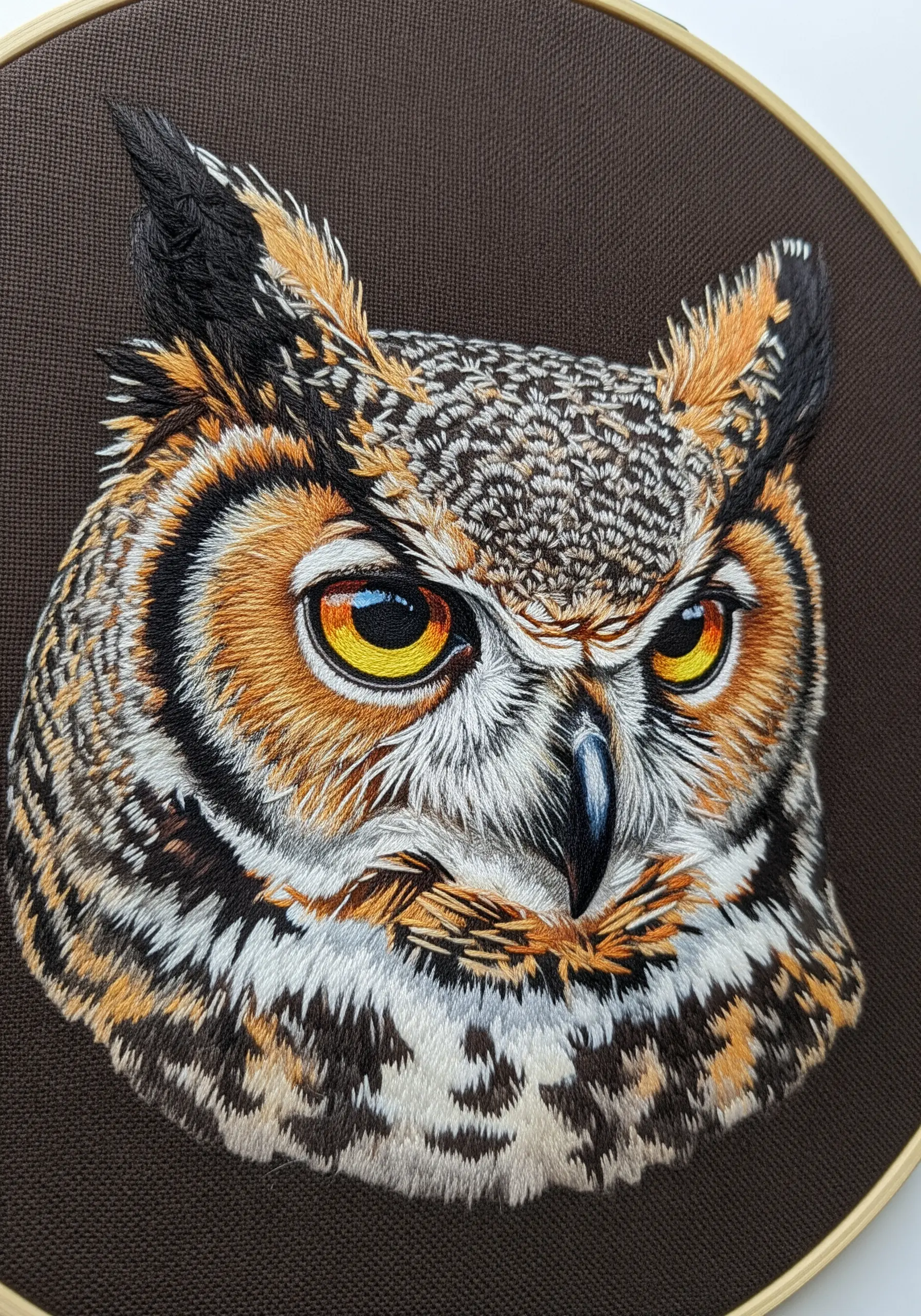 A hyper-realistic, close-up portrait of a horned owl's face, showcasing detailed thread painting.