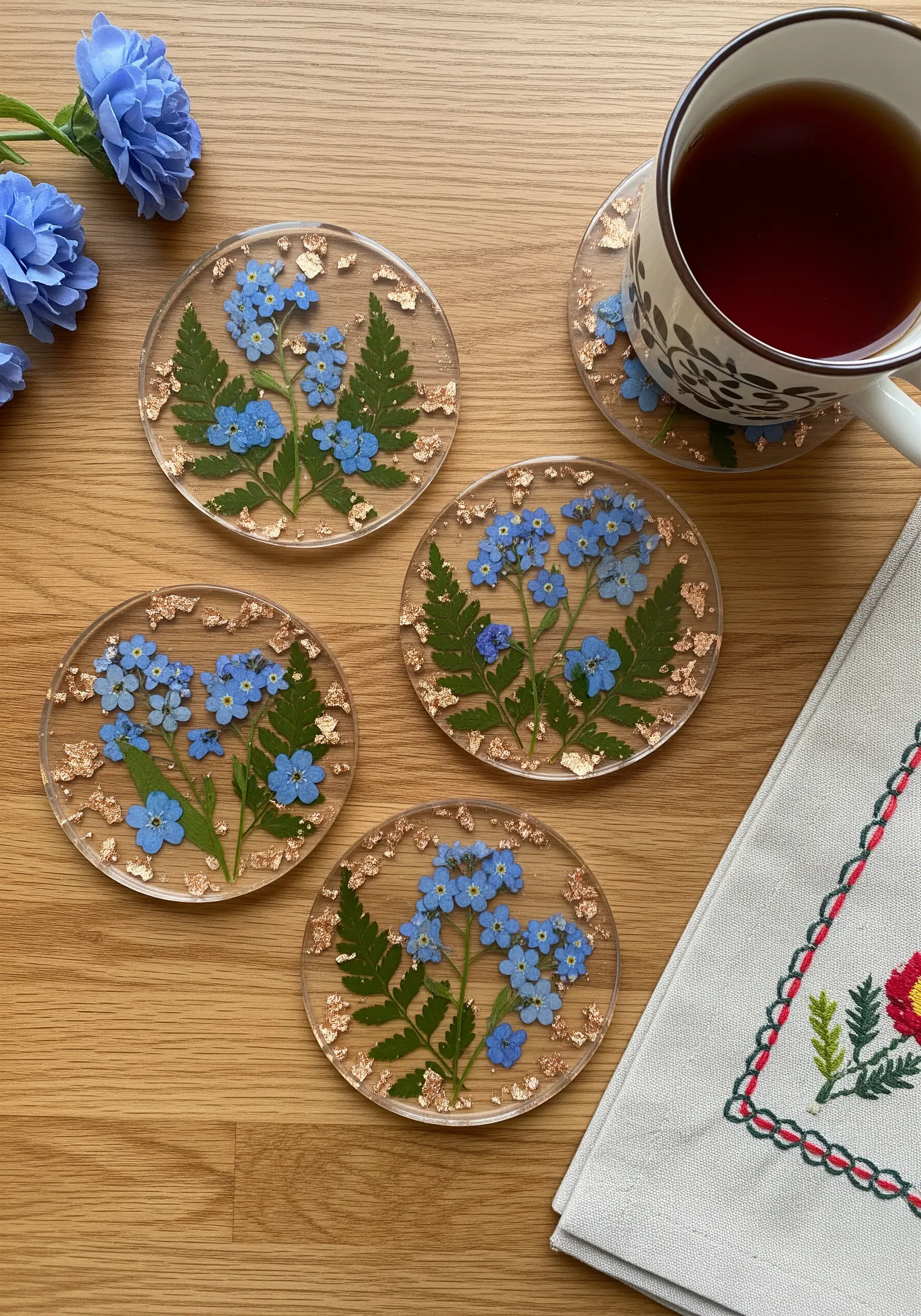 Four coasters with pressed blue forget-me-nots and gold flakes, inspiring a sheer fabric embroidery idea.
