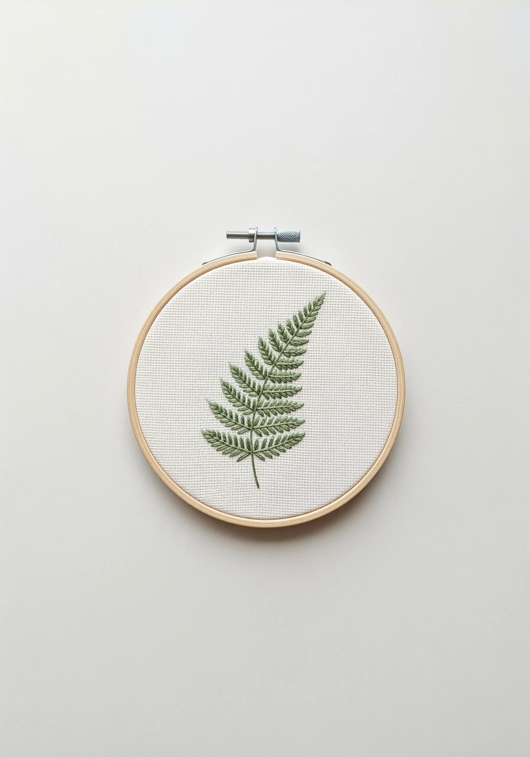 Finely detailed embroidered fern leaf in a wooden embroidery hoop on a white background.