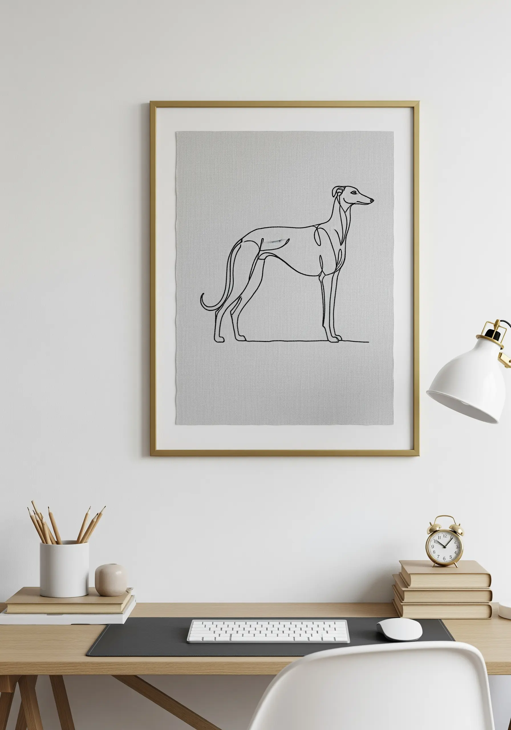 A single-line art embroidery of a greyhound dog, framed and placed on a desk.