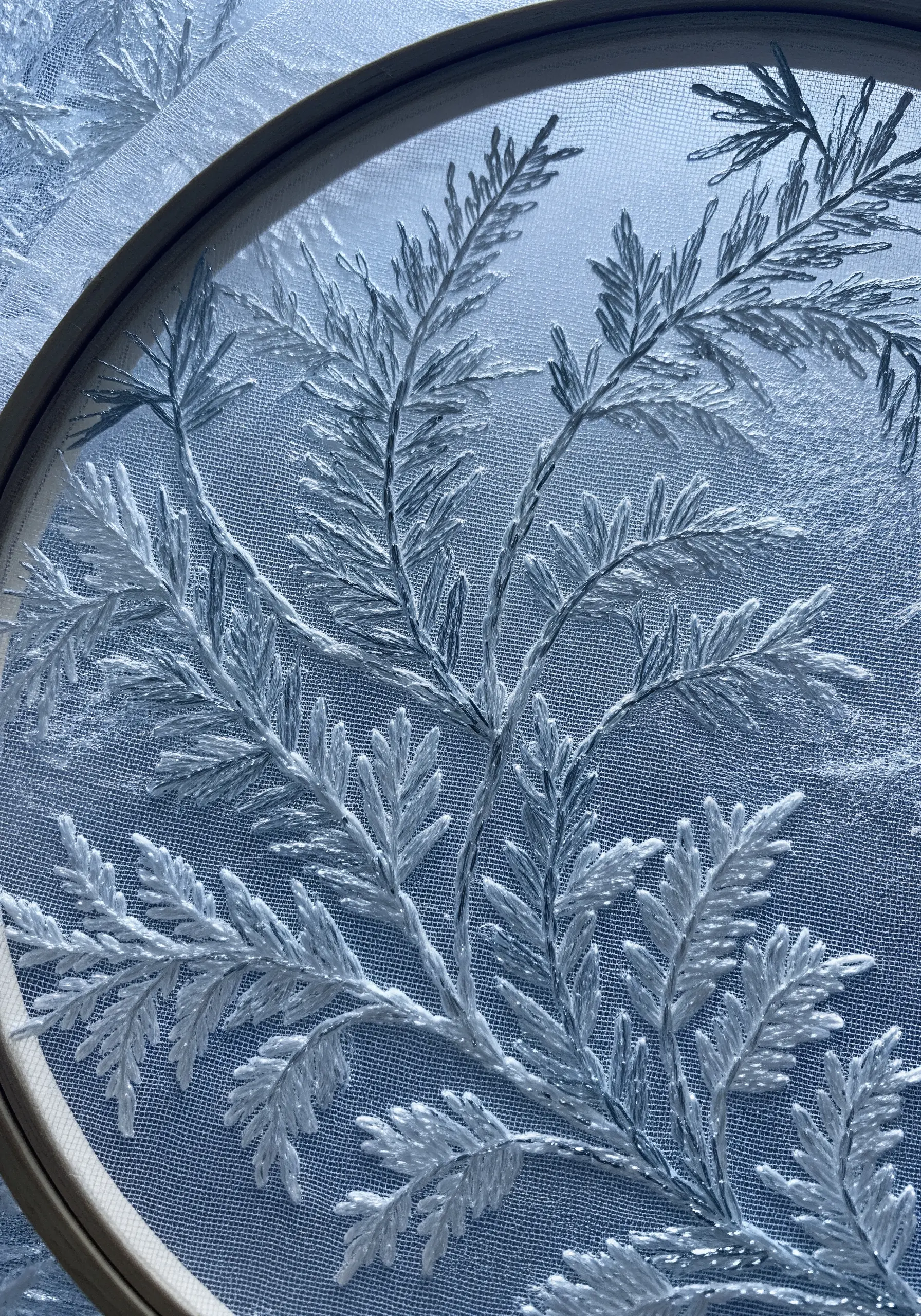Delicate white embroidery of frost patterns on a sheer, light blue fabric like organza.