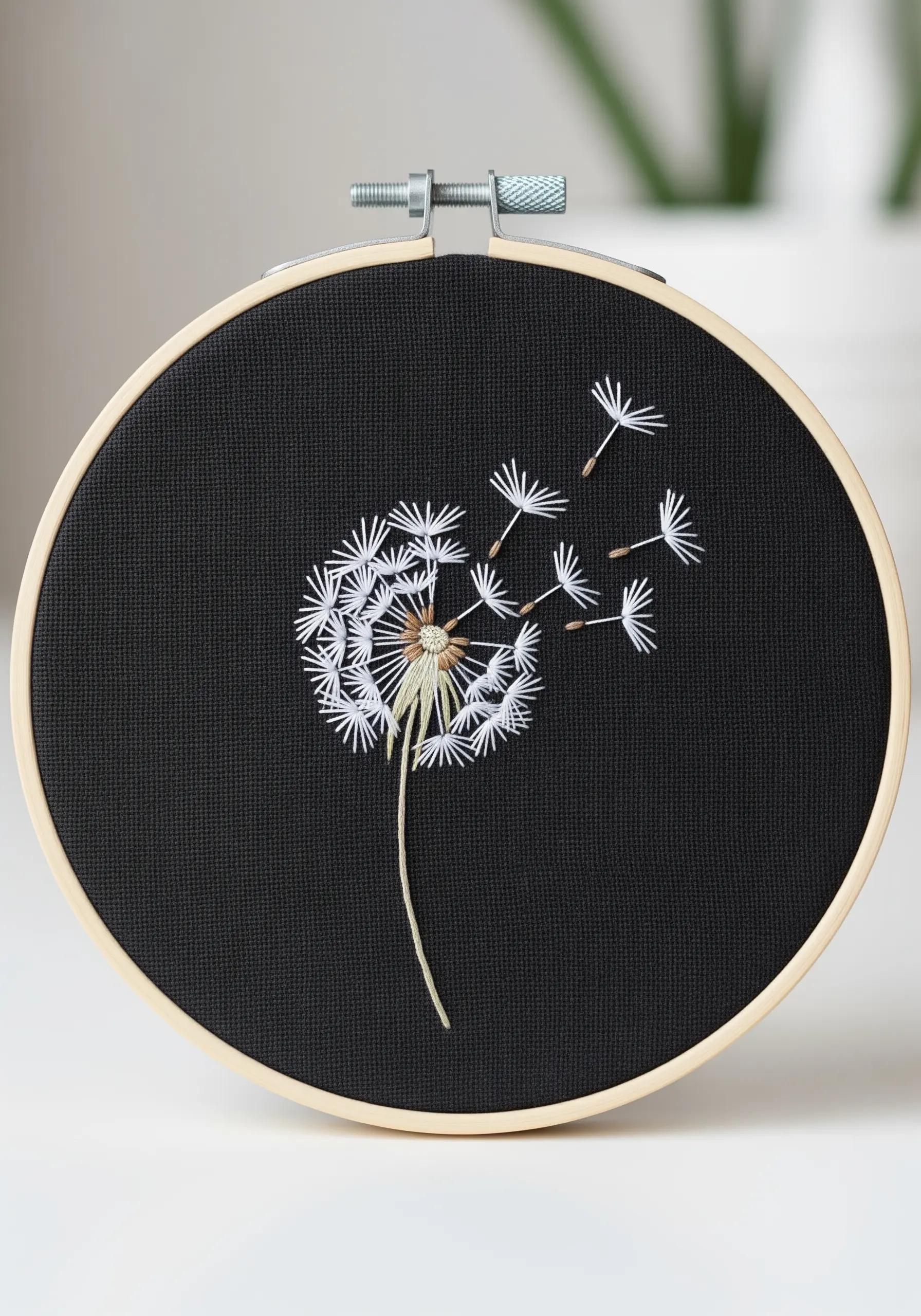 Dandelion head with seeds blowing away, embroidered in white on black fabric