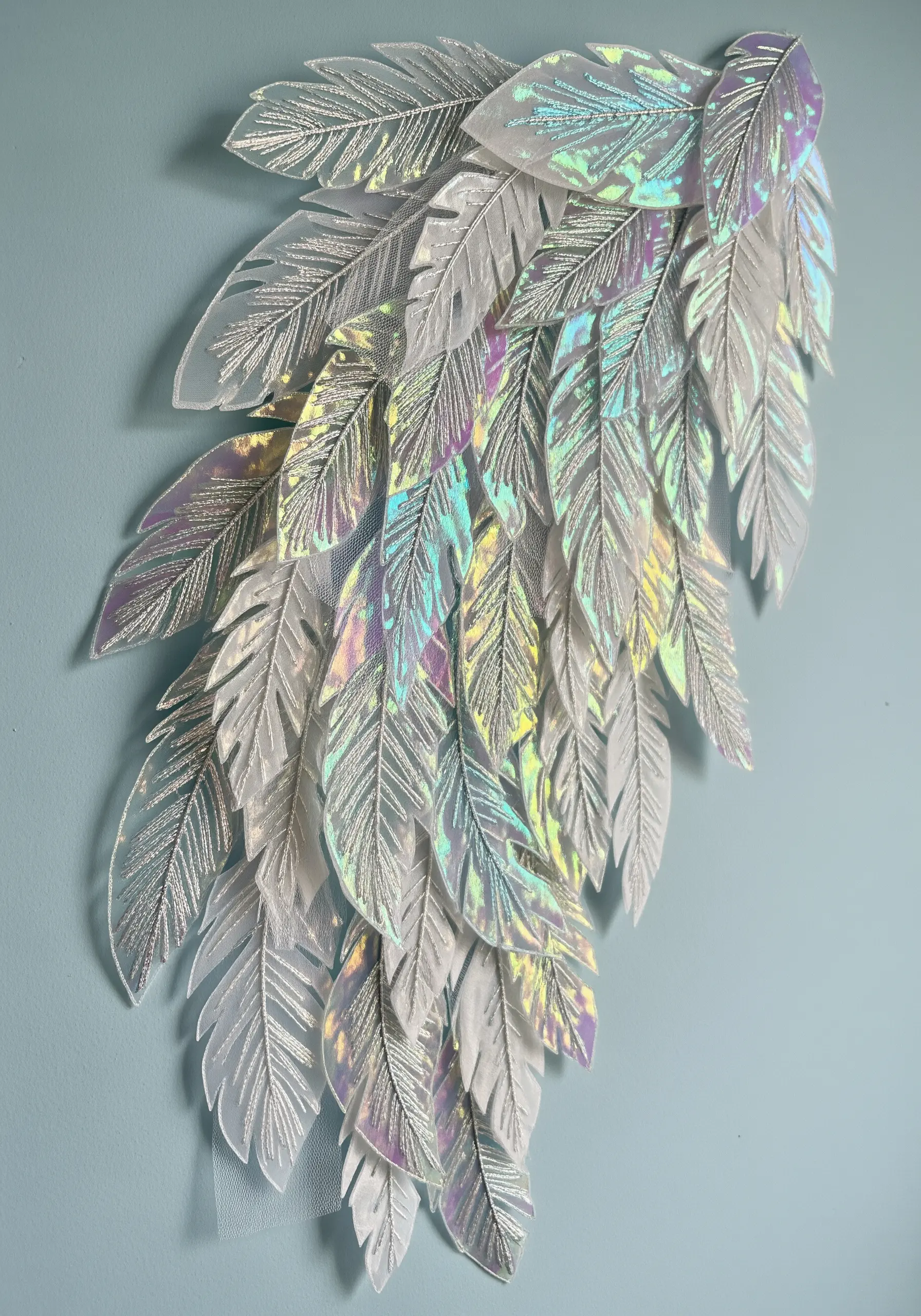 A sculpture of layered wings made from iridescent and white sheer fabrics, stitched with silver thread.