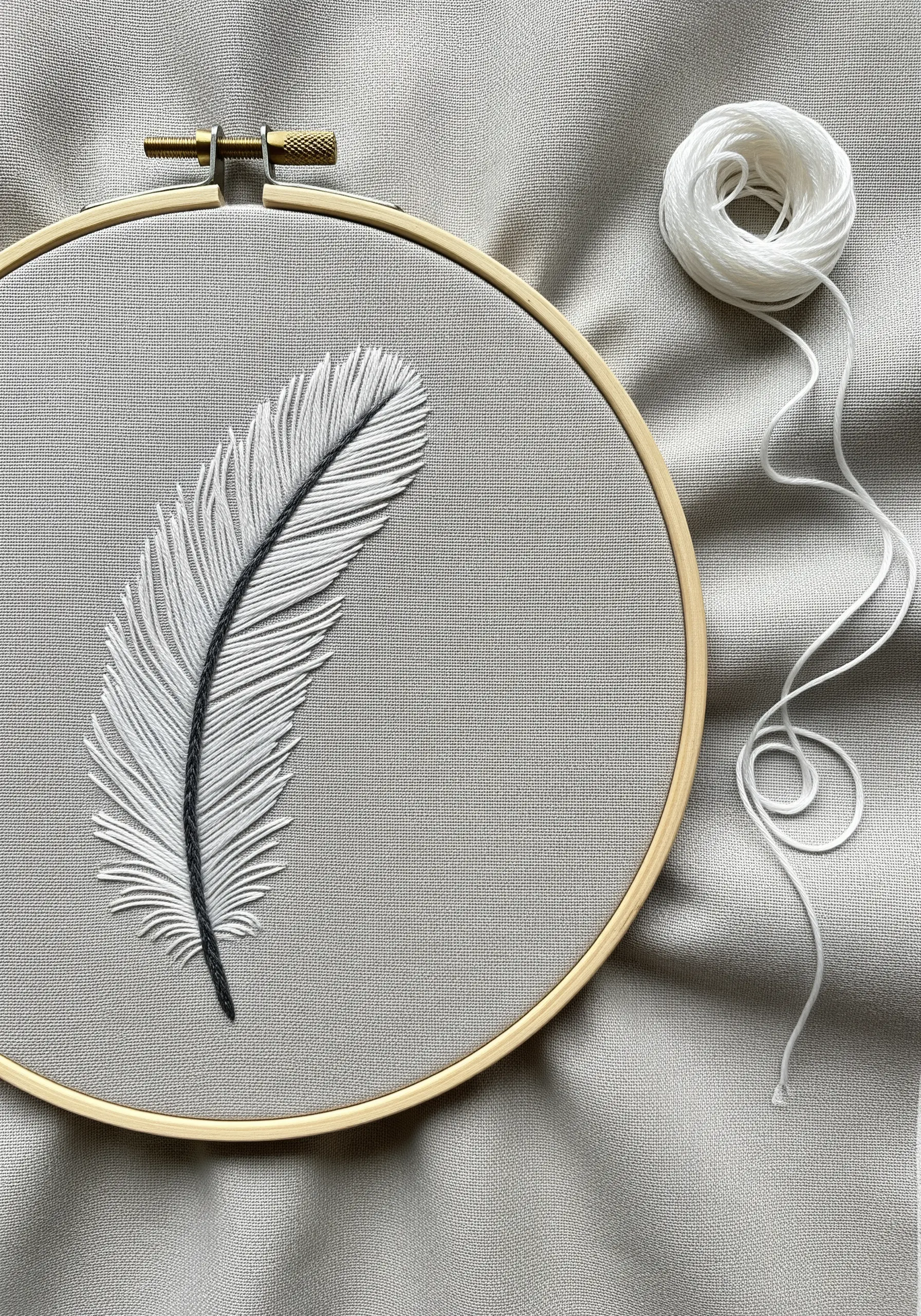 A realistic white feather with a dark spine, embroidered on grey fabric.