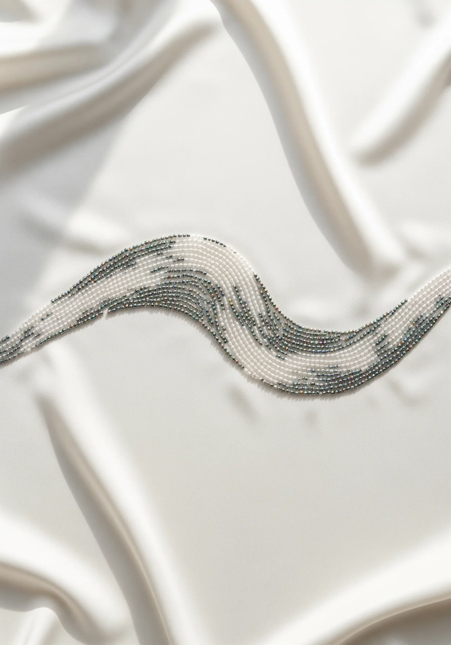 A flowing wave shape created with densely packed seed beads in white and grey on white silk.