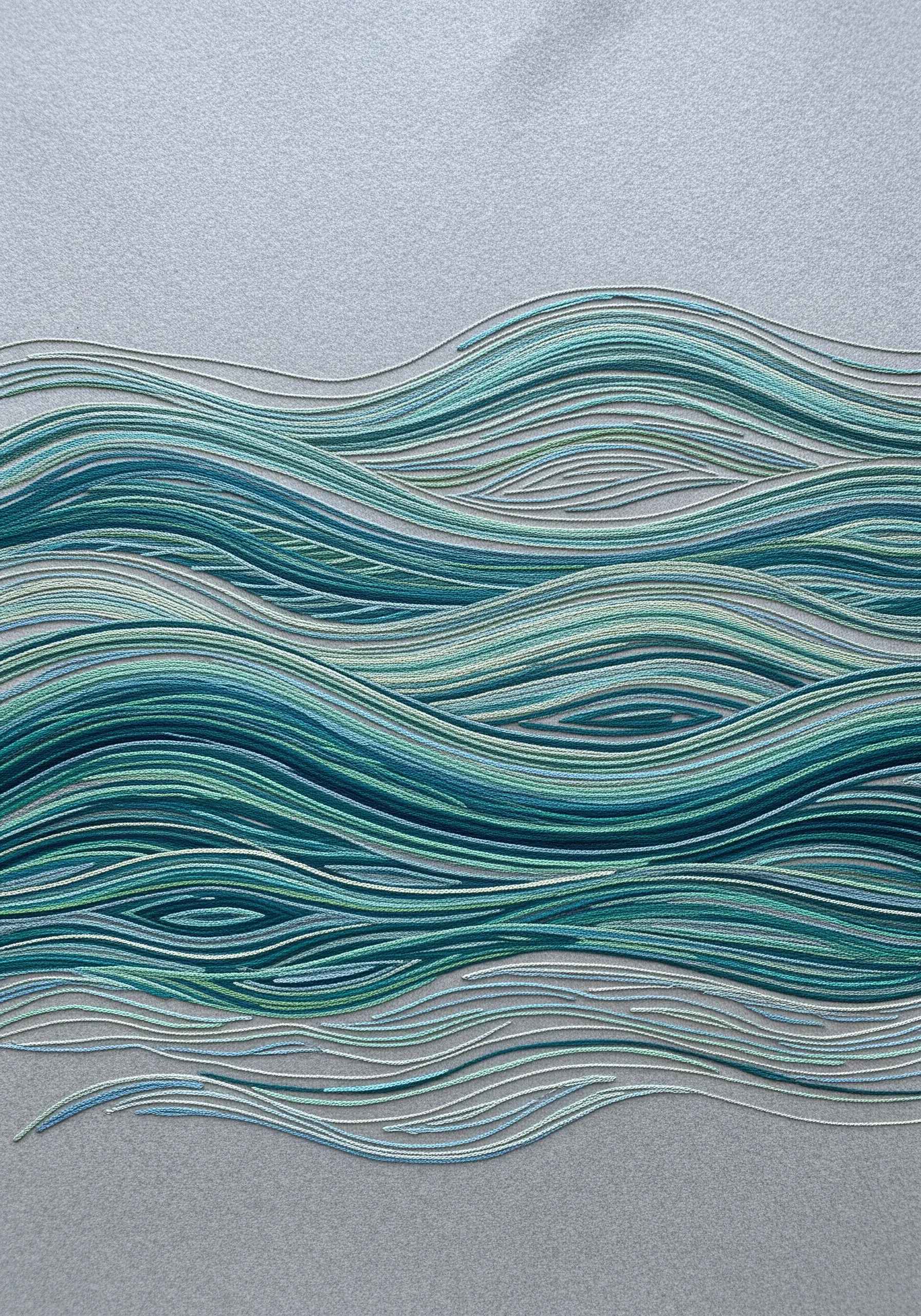 Abstract embroidered waves in flowing parallel lines of blue, green, and white thread.
