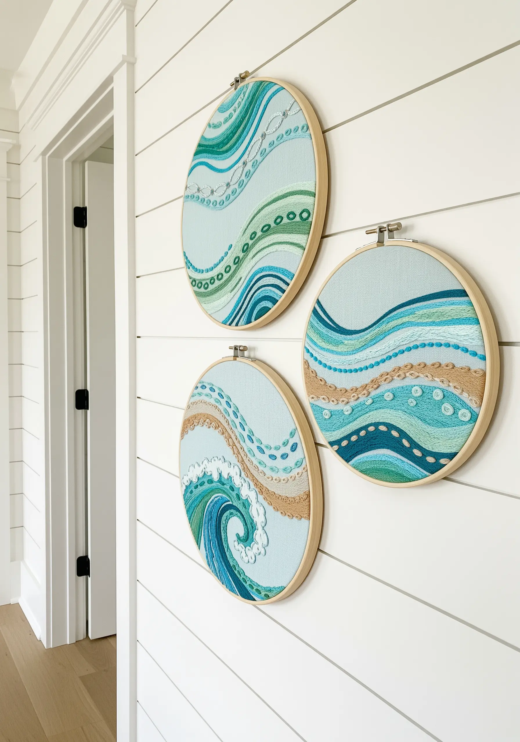 Three oval embroidery hoops with abstract ocean wave patterns in blue, green, and sand tones.