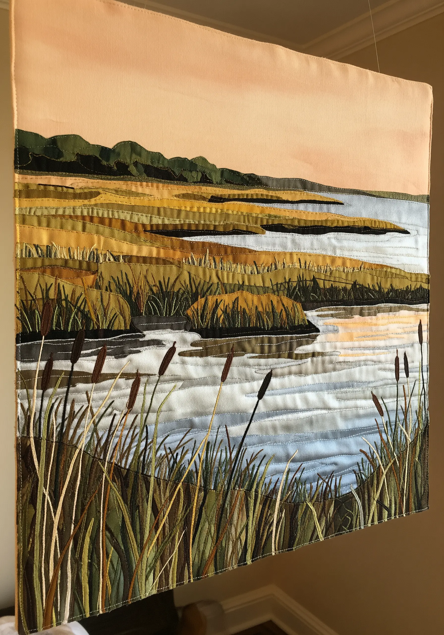 A fabric collage wall hanging of a marshland scene at sunset, with embroidered cattails.