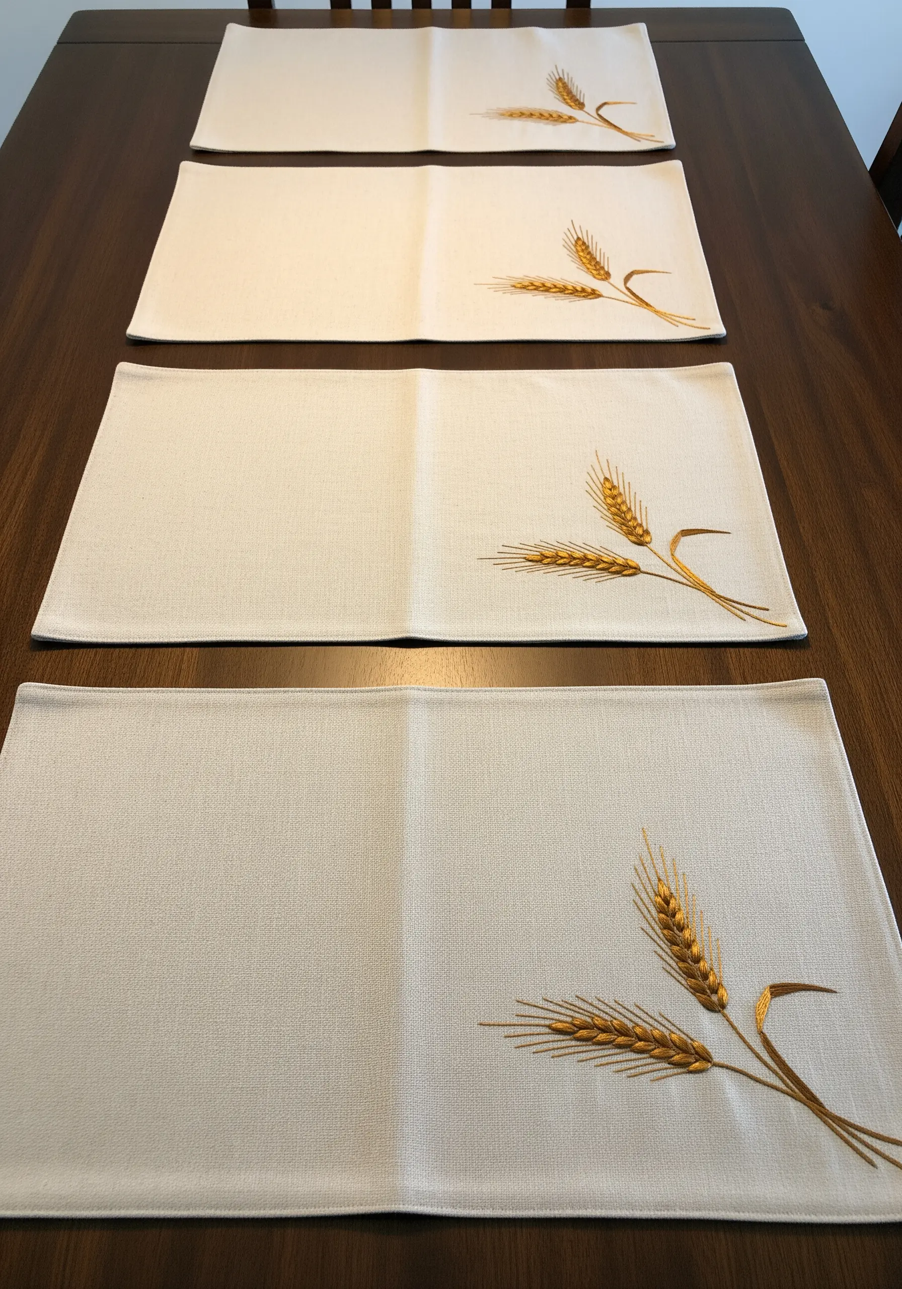 Linen placemats on a wooden table, each with a golden embroidered wheat stalk.