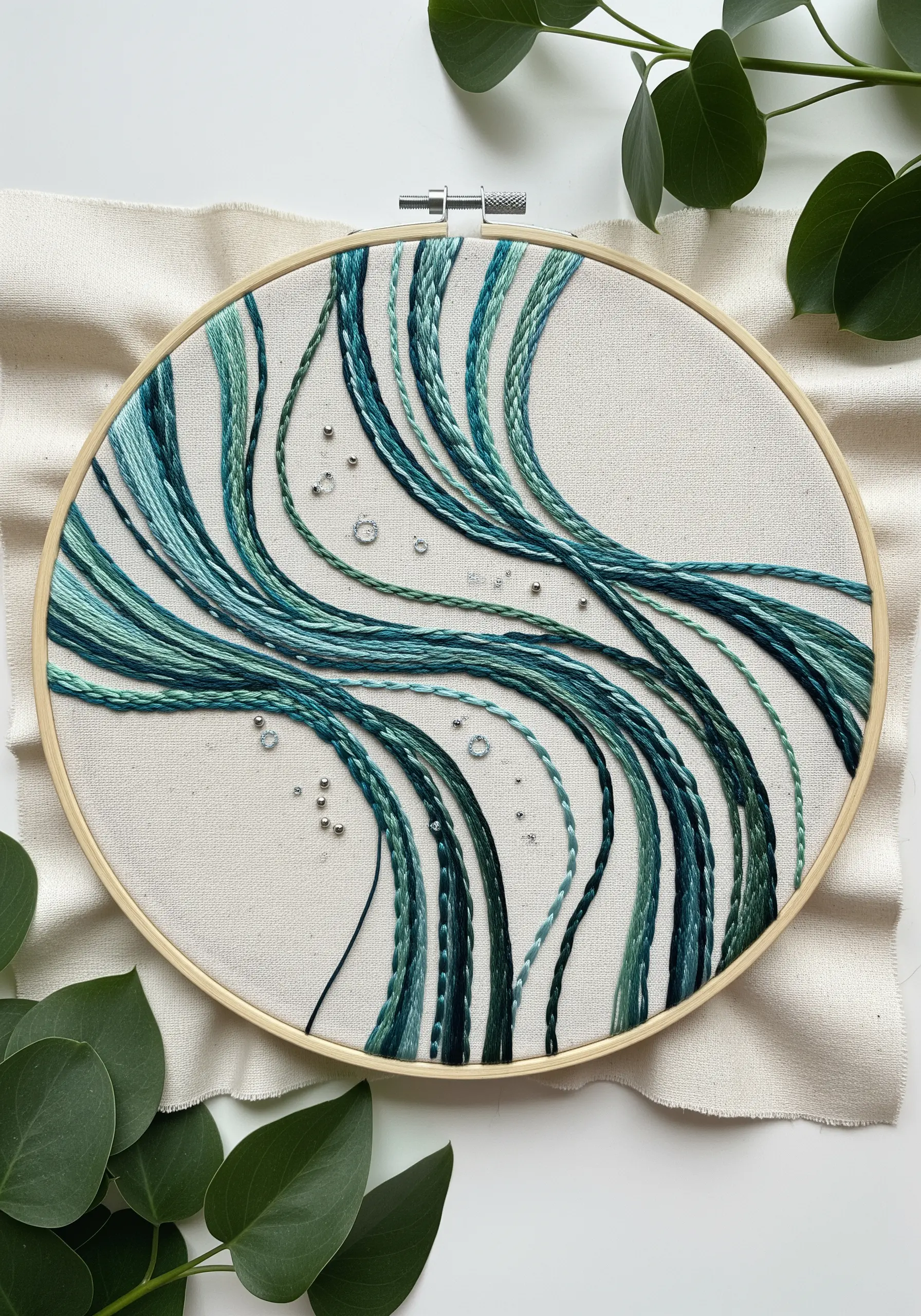 Abstract hoop art with flowing teal and green threads and silver beads.